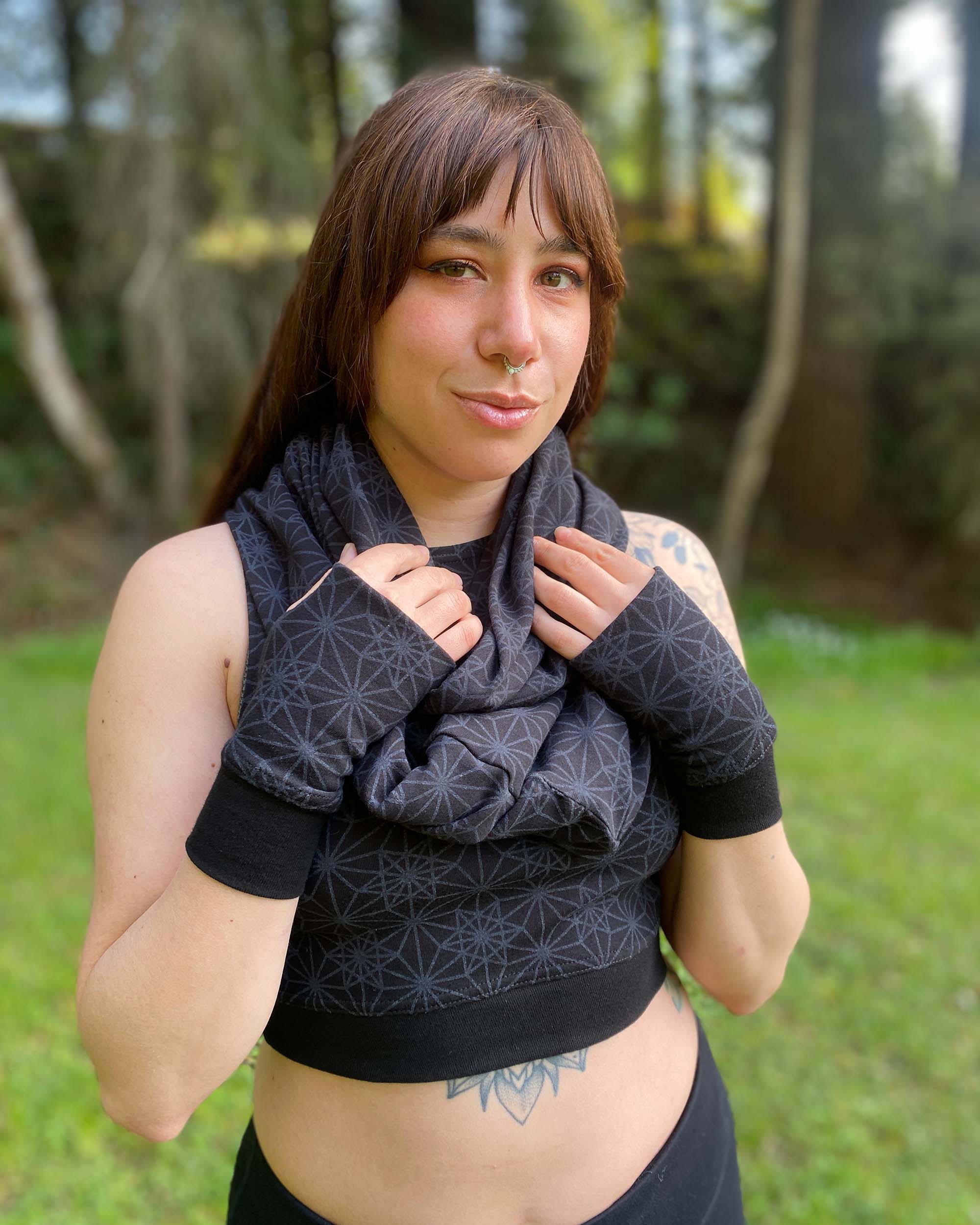 Organic cotton hand warmers and matching scarf in black fabric and geometric print, worn by female model in nature.