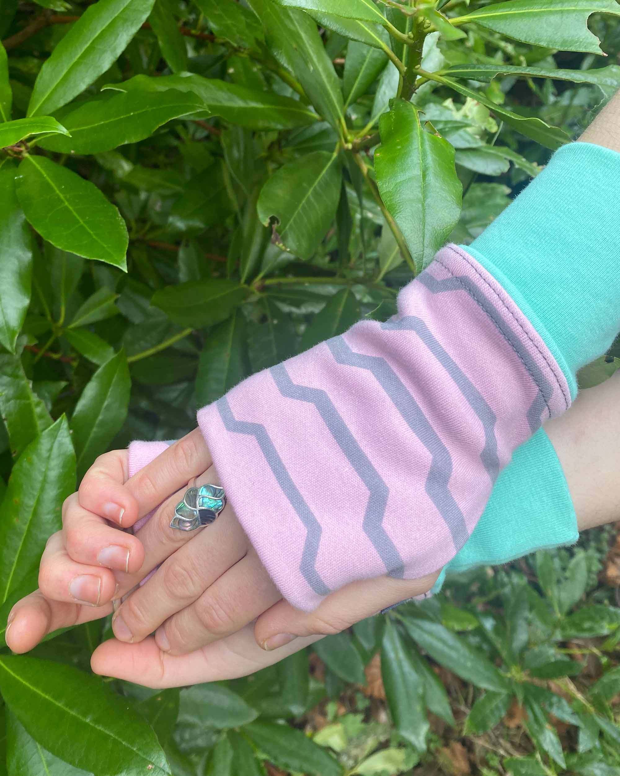 Organic cotton fingerless gloves in pink fabric with geometric print and green accents.