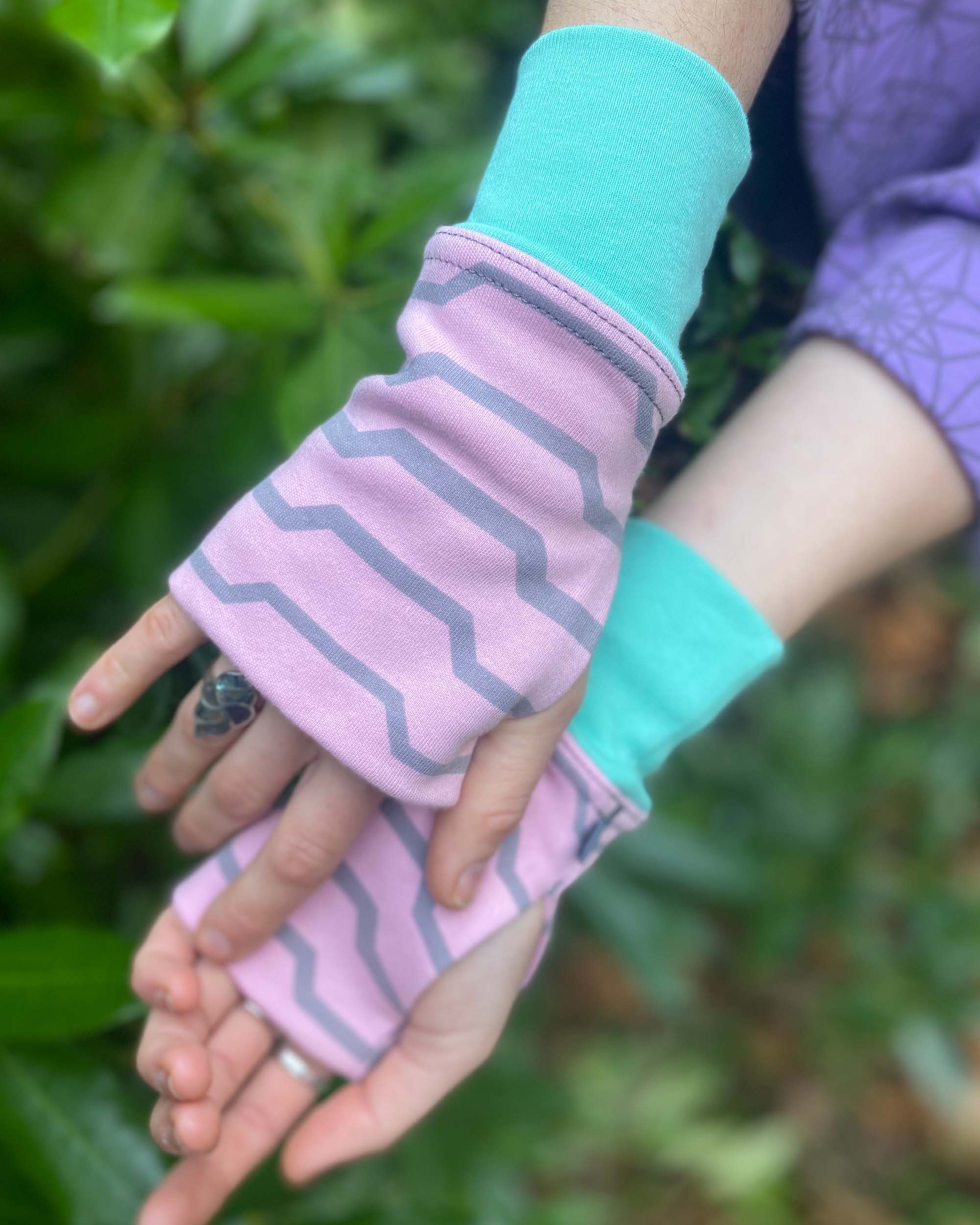 Organic cotton fingerless gloves in pink fabric with geometric print, right hand view in nature.