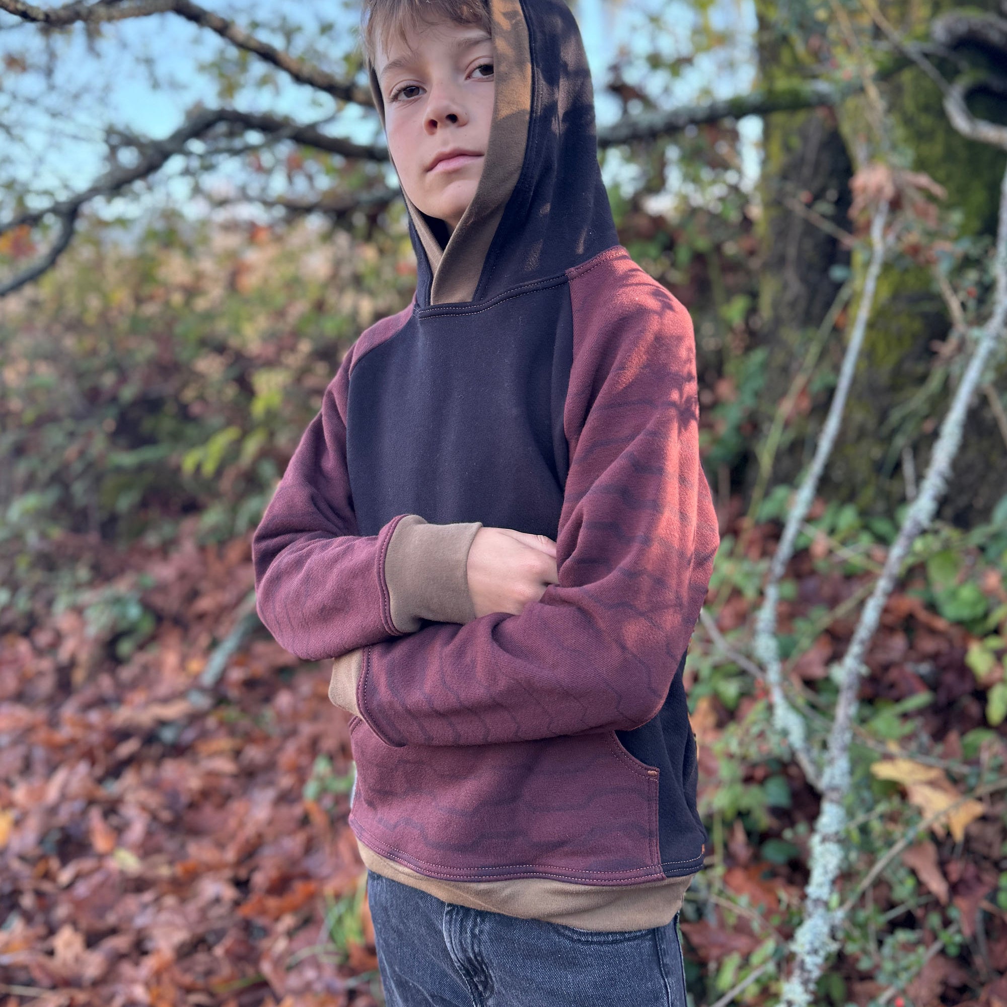 Organic cotton youth fleece hoodie, black and brown color with geometric printed sleeves, worn by a boy in fall.