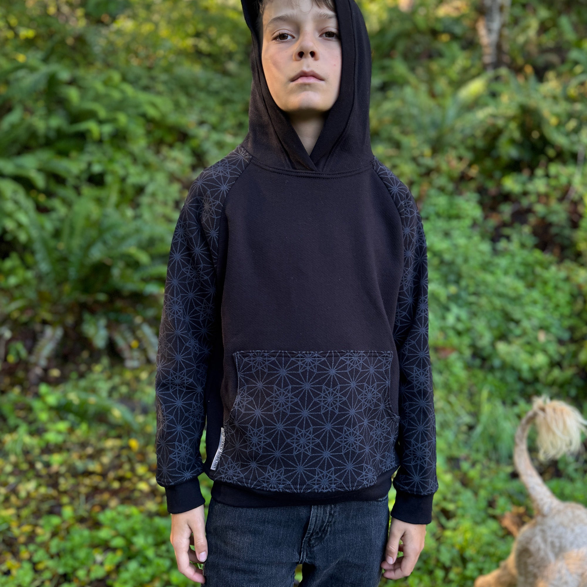 Organic cotton youth fleece hoodie, black with geometric printed sleeves, front view worn by a boy in nature.