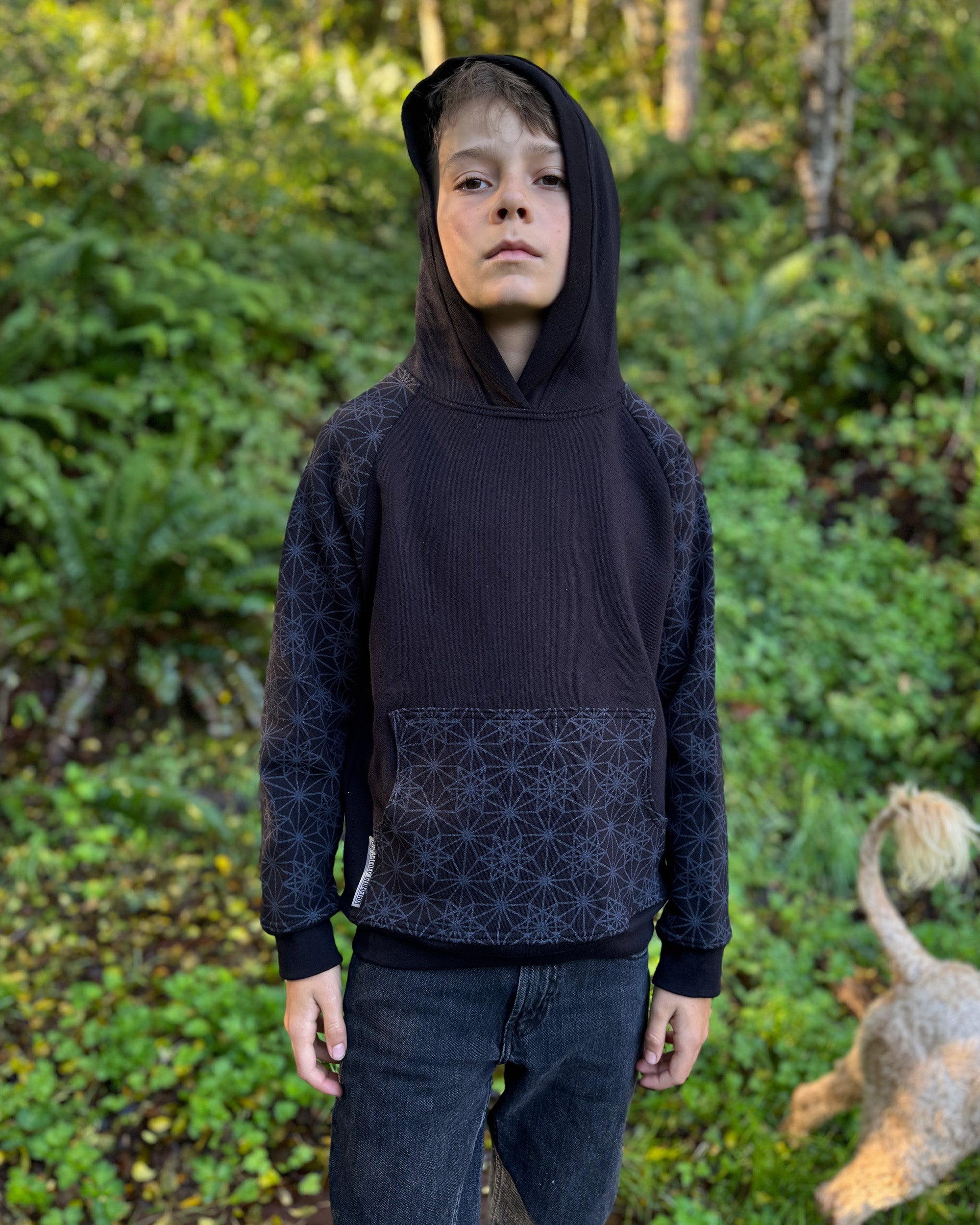 Organic cotton youth fleece hoodie, black with geometric printed sleeves, front view worn by a boy in nature.