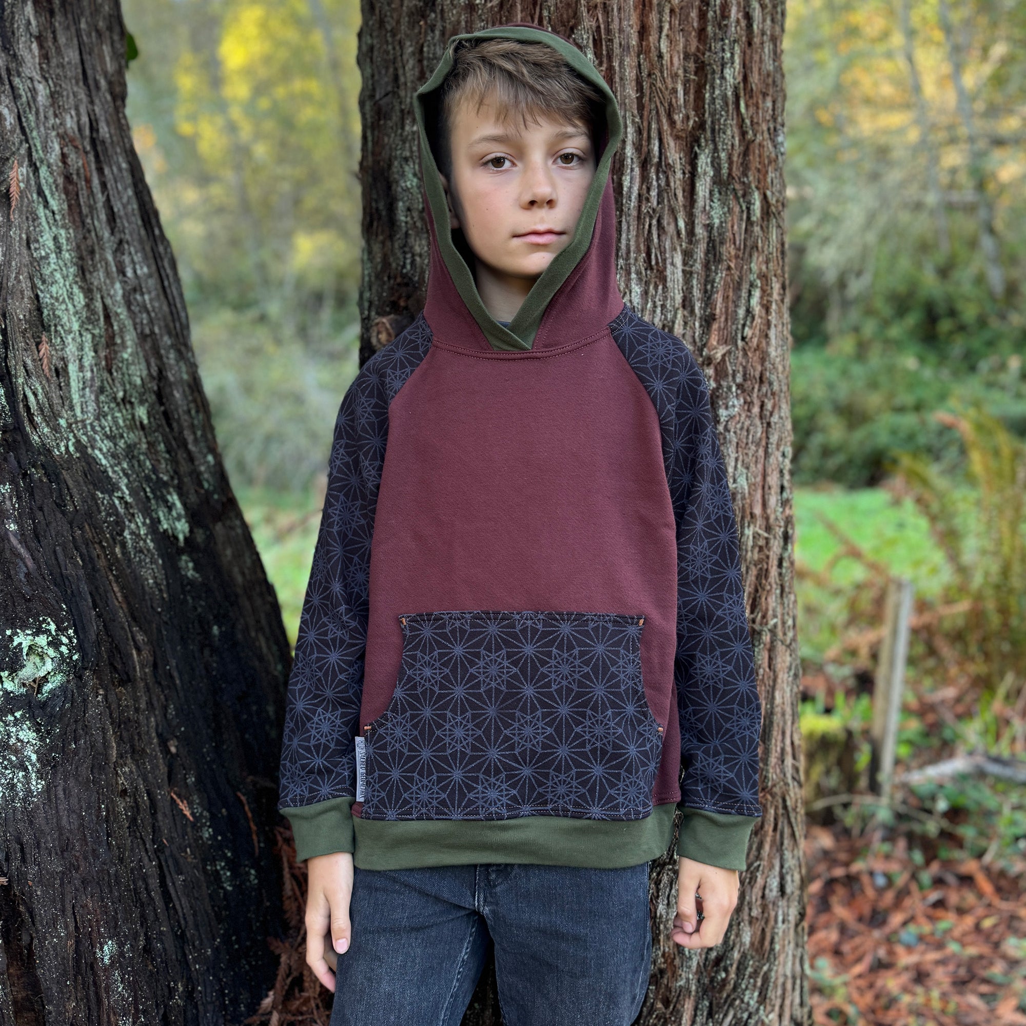 Fleece youth hoodie, black fabric with geometric print, front view on boy model with trees.