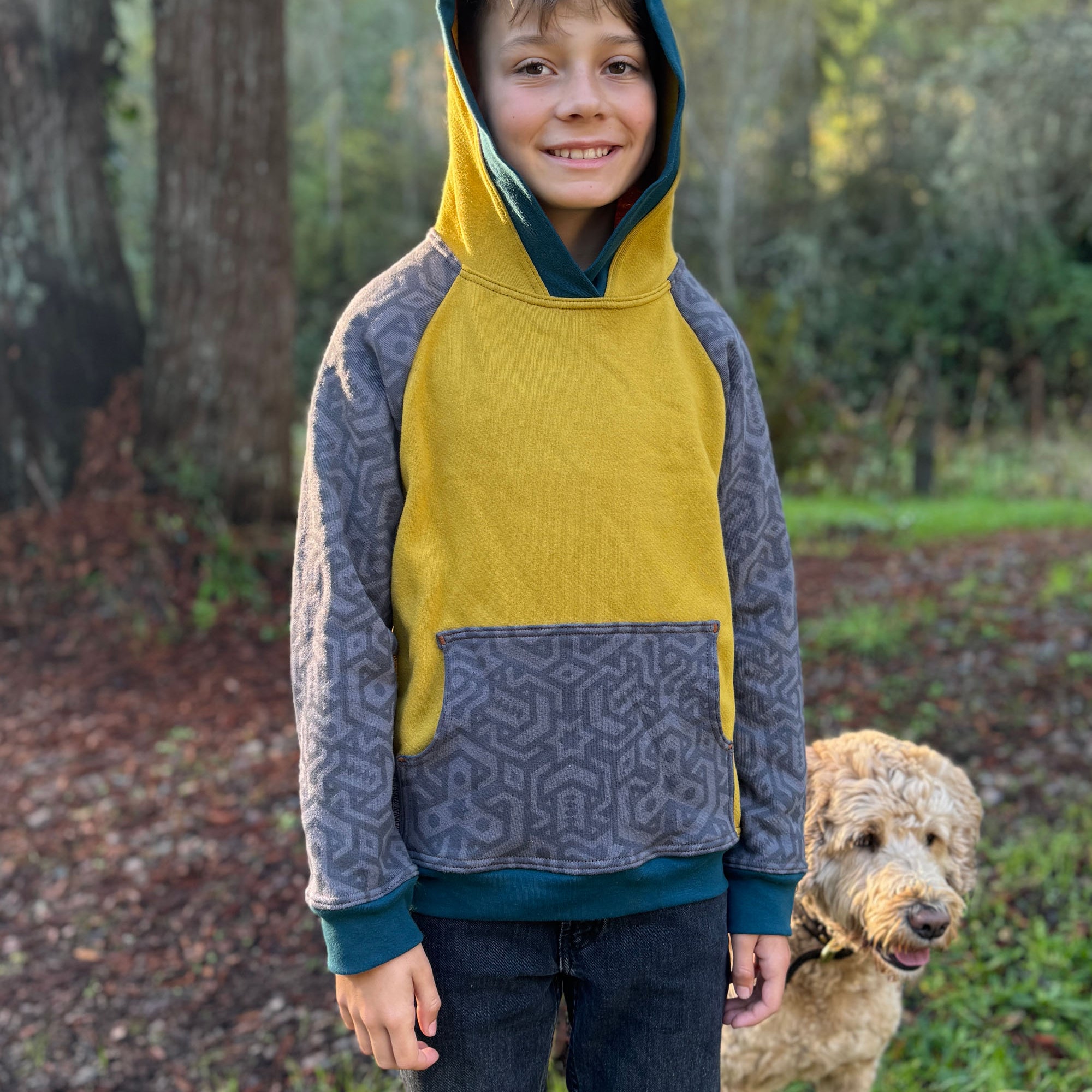 Organic cotton fleece kids hoodie, yellow and grey fabric with geometric print, worn by a smiling boy.