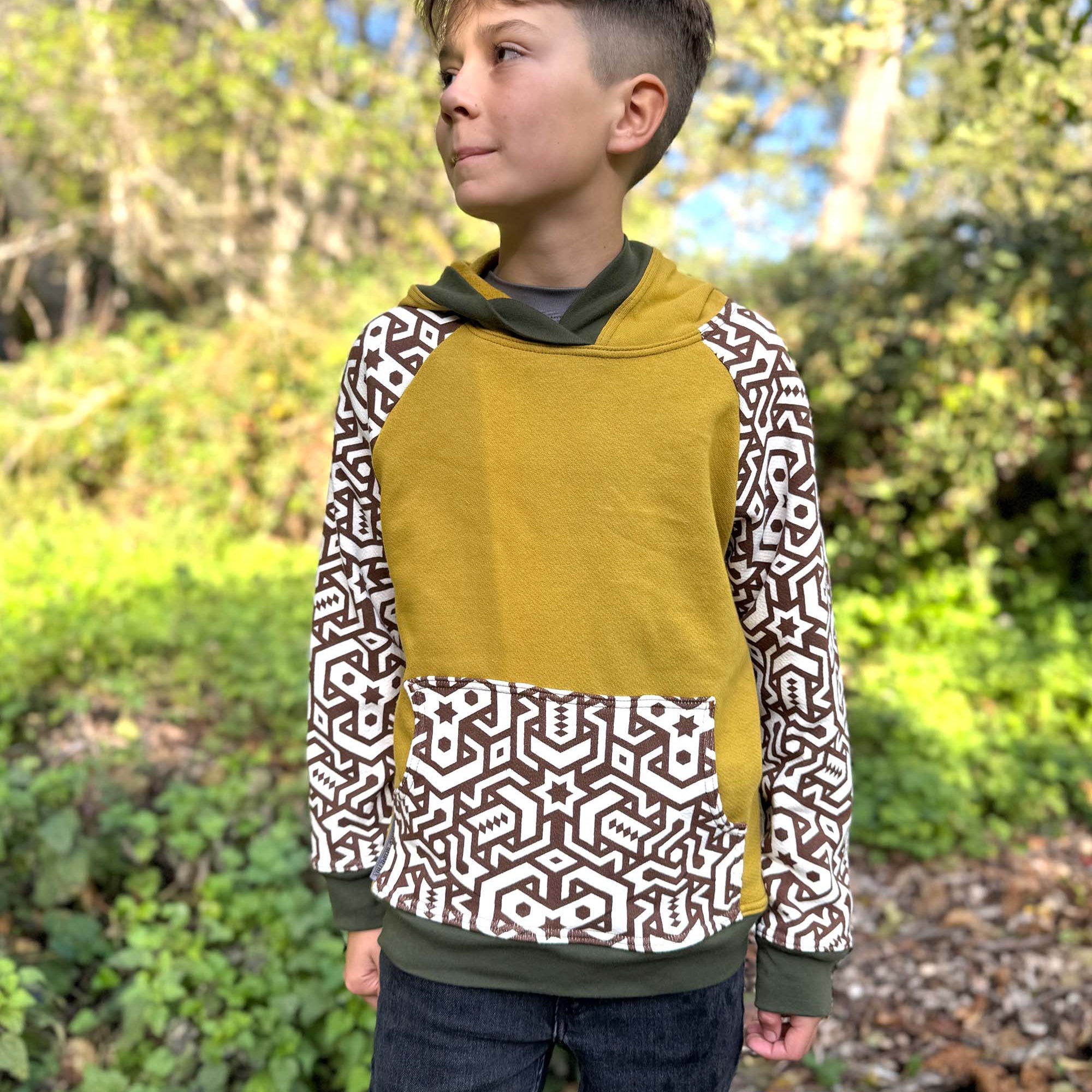 Organic cotton kids hoodie, yellow with geometric printed sleeves, front view, worn by a boy in nature.
