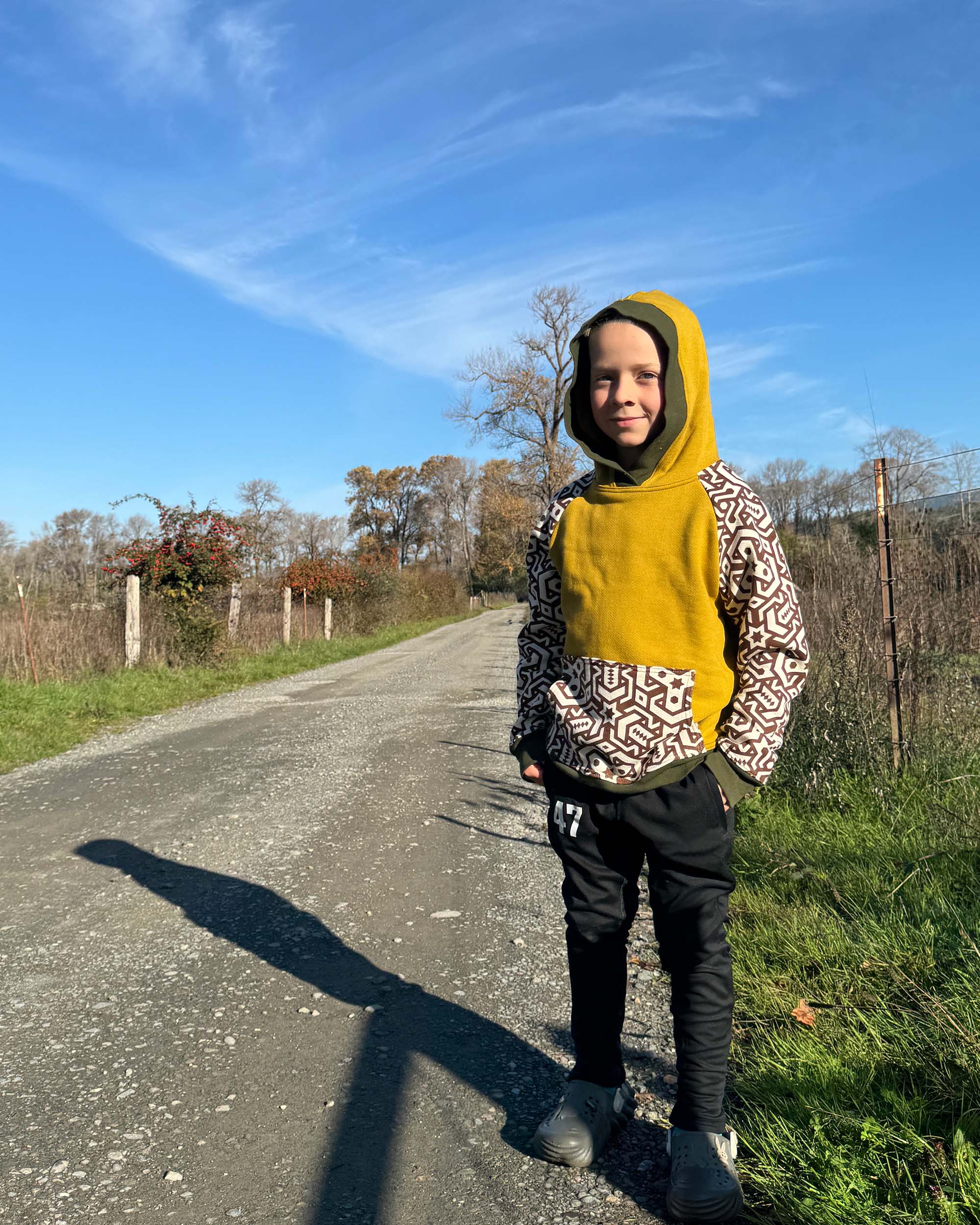 Organic cotton kids hoodie, yellow with geometric printed sleeves, front view, worn by a small boy.