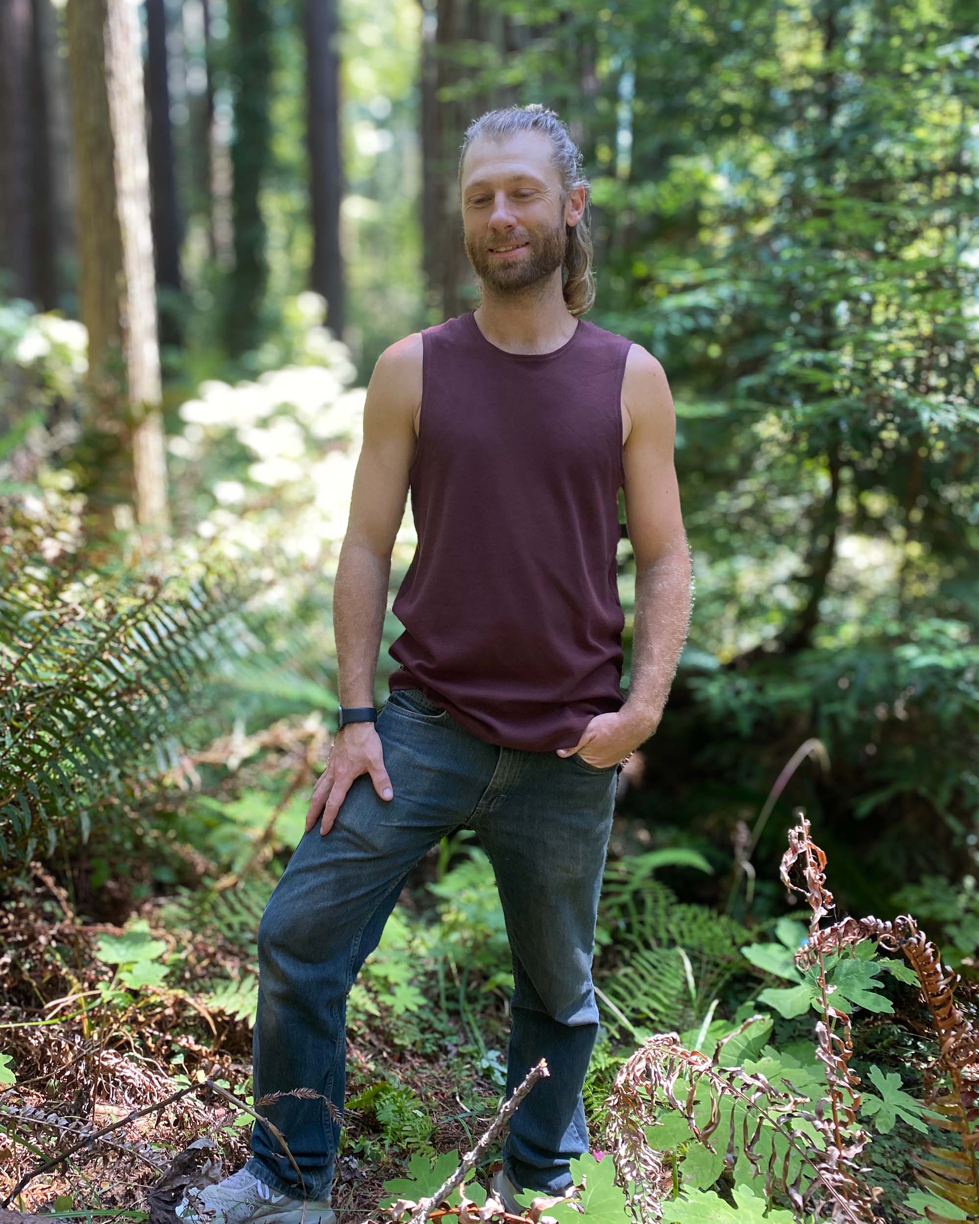 Organic cotton mens tank top, brown fabric, front view on model in trees.