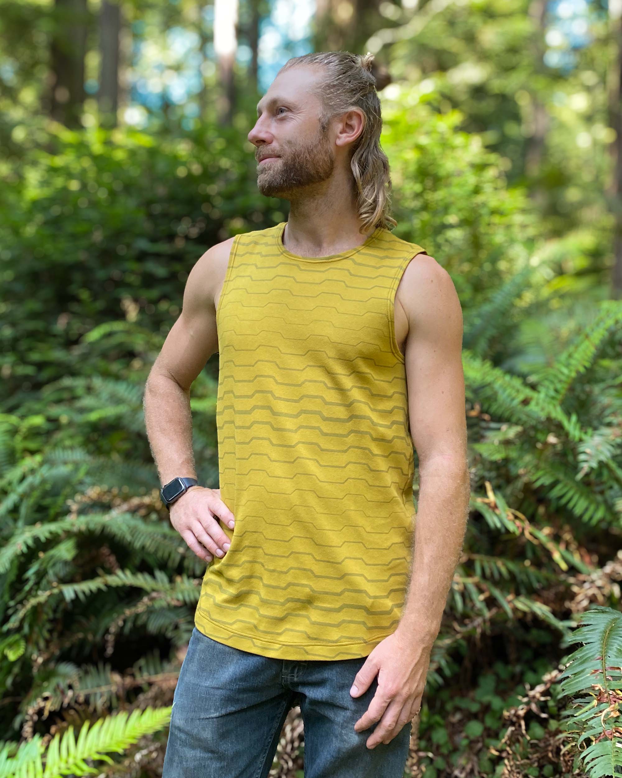 Organic cotton mens tank top, yellow fabric with geometric print, left side view outdoors.
