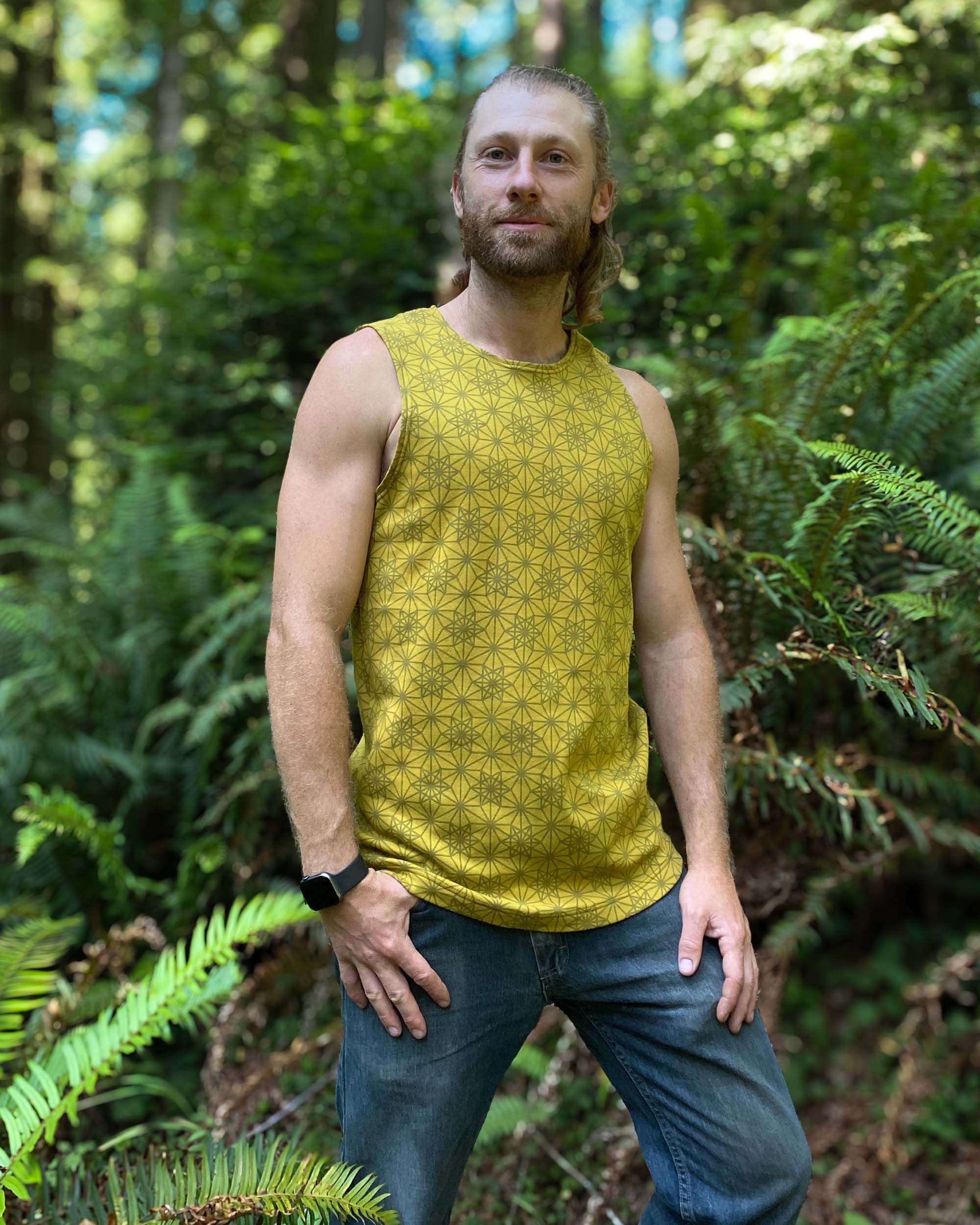 Organic cotton mens tank top, yellow fabric with geometric print, left side view with model in natural light.