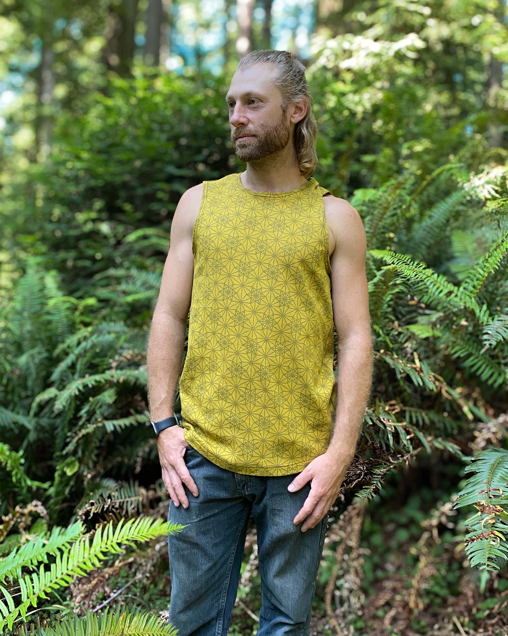 Organic cotton mens tank top, yellow fabric with geometric print, right side view with model in natural light.