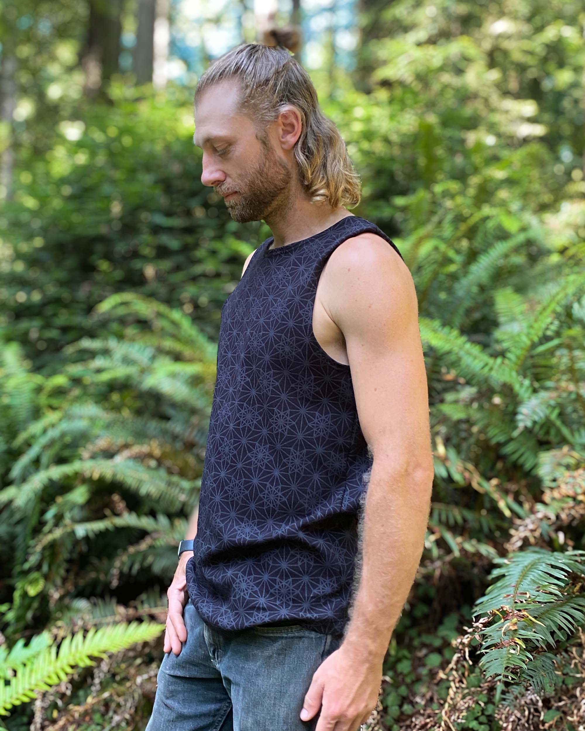 Organic cotton mens tank top, black fabric with geometric print, side view with model in natural light.