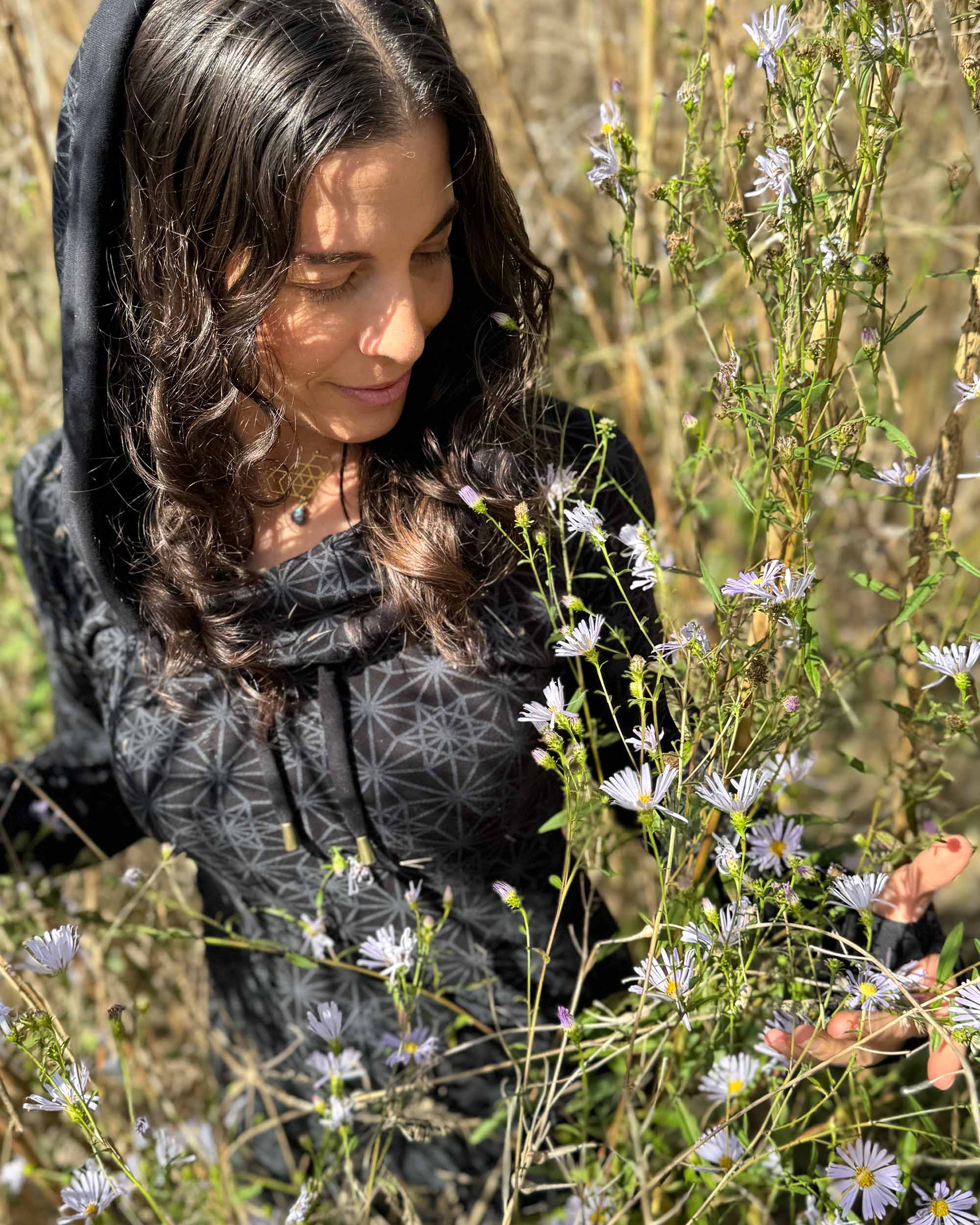 Organic cotton long sleeve tunic dress, black with sacred geometry print, front view on female model with flowers.