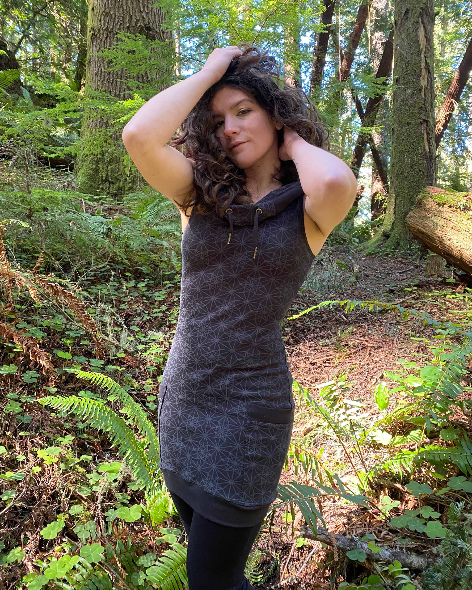 Organic cotton sleeveless hooded dress, black fabric with geometric print, front view on female model.