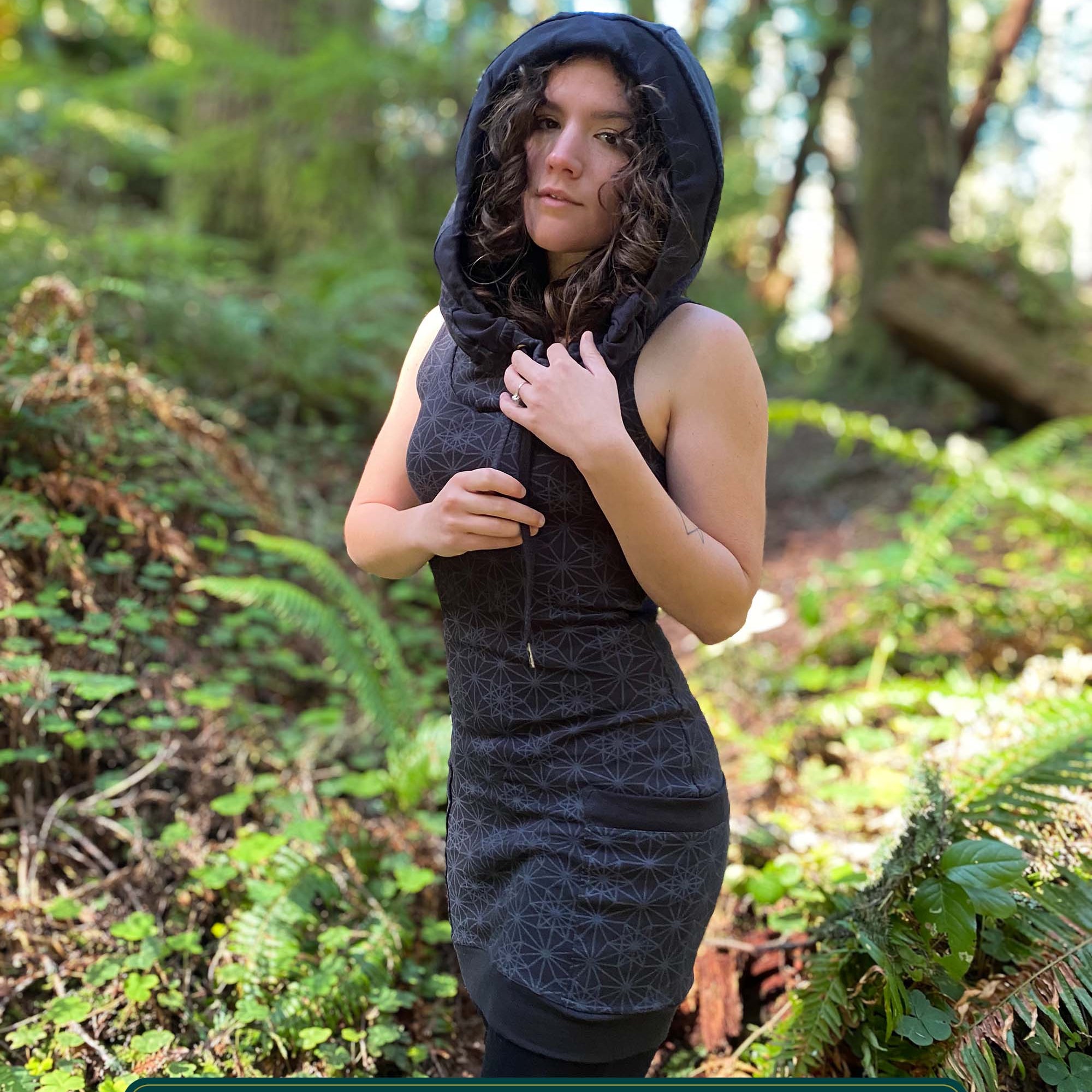 Organic cotton sleeveless hooded dress, black fabric with geometric print, front left side view on female model.