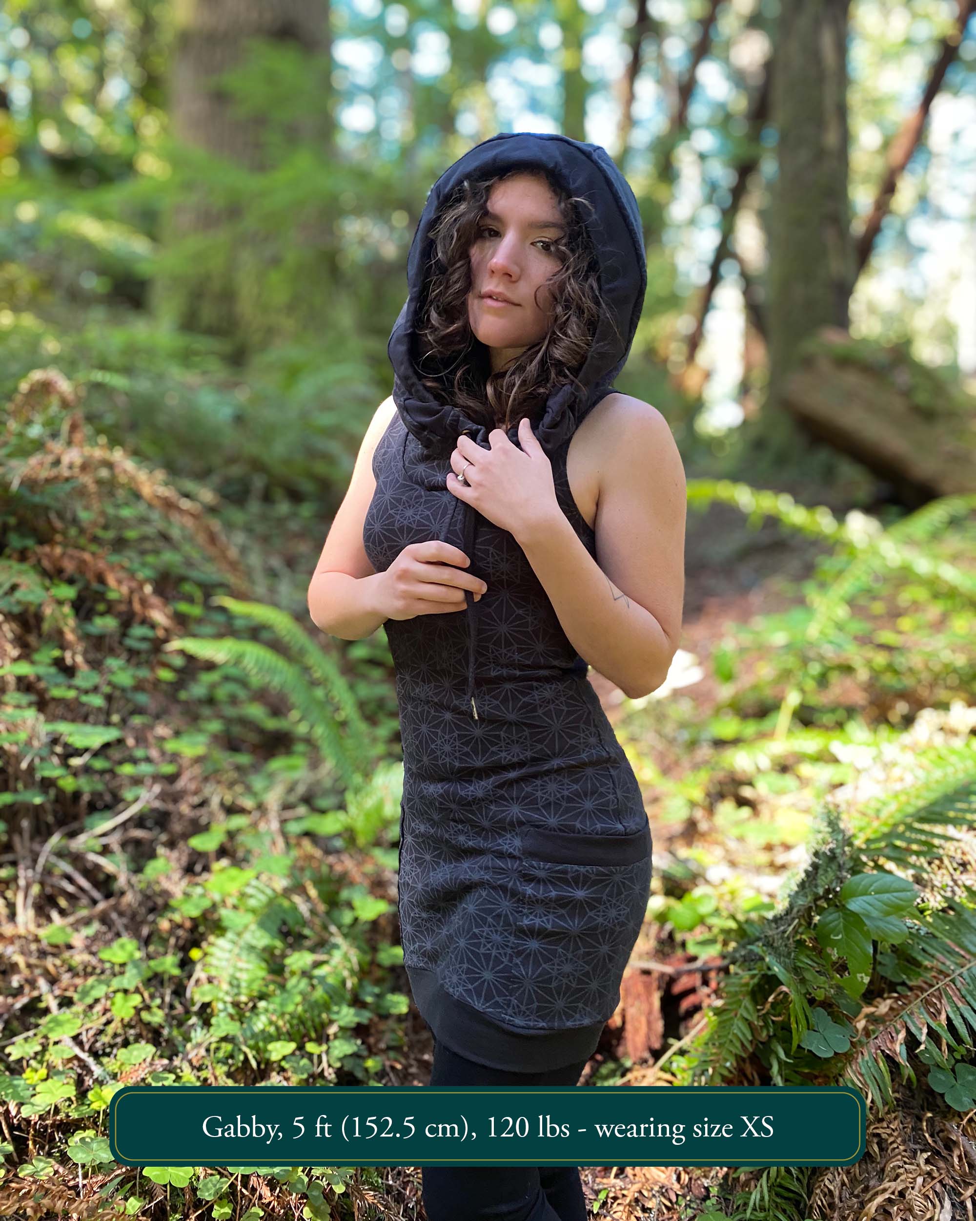 Organic cotton sleeveless hooded dress, black fabric with geometric print, front left side view on female model.