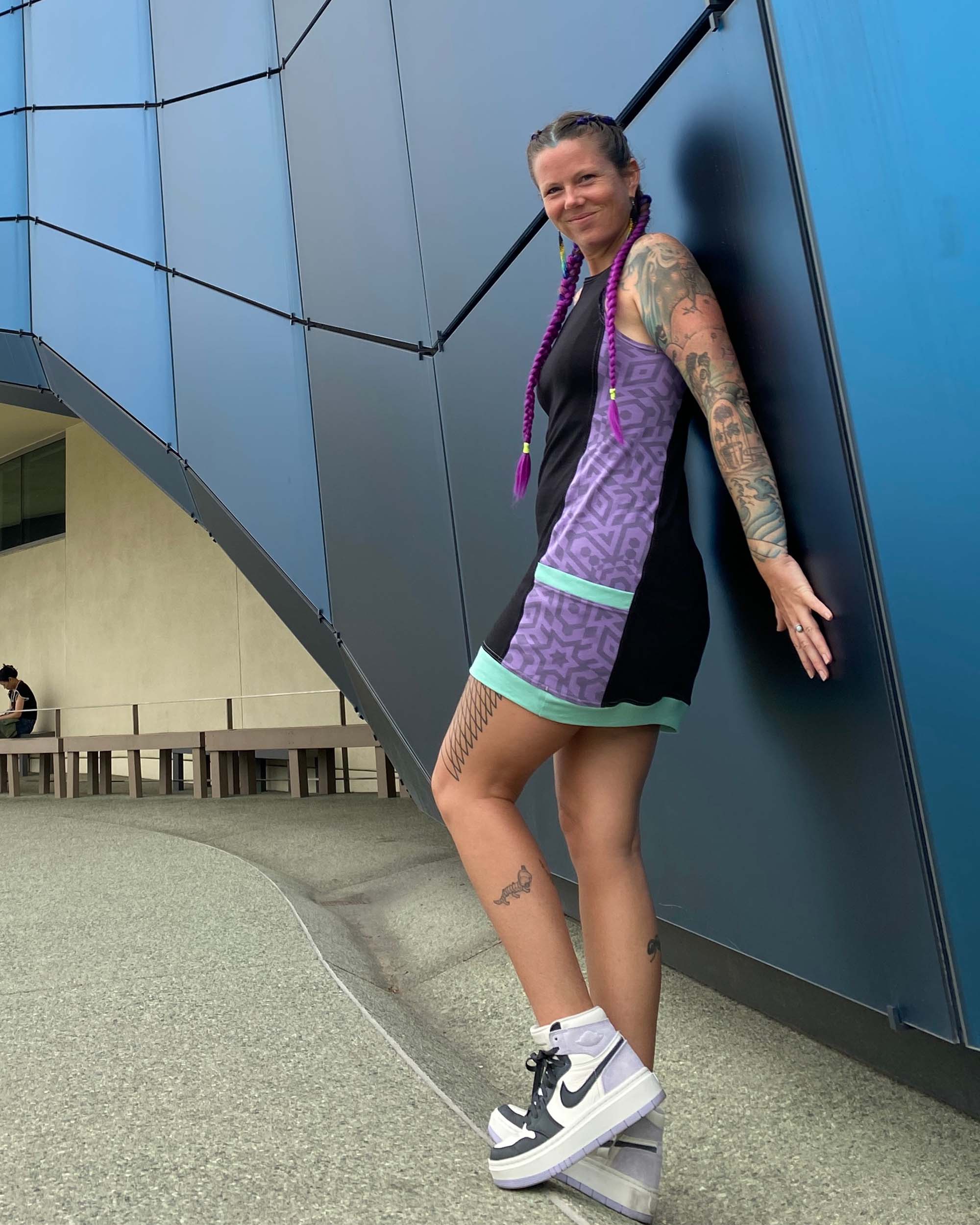 Organic cotton sleeveless dress, black fabric with lavender accent fabric and geometric print, on female model.