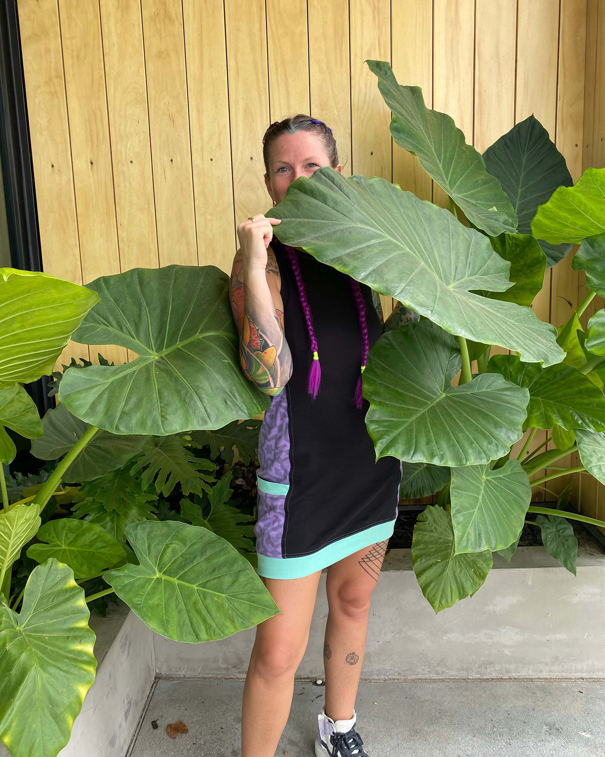 Organic cotton sleeveless dress, black fabric with lavender accent fabric and geometric print, on model in nature.