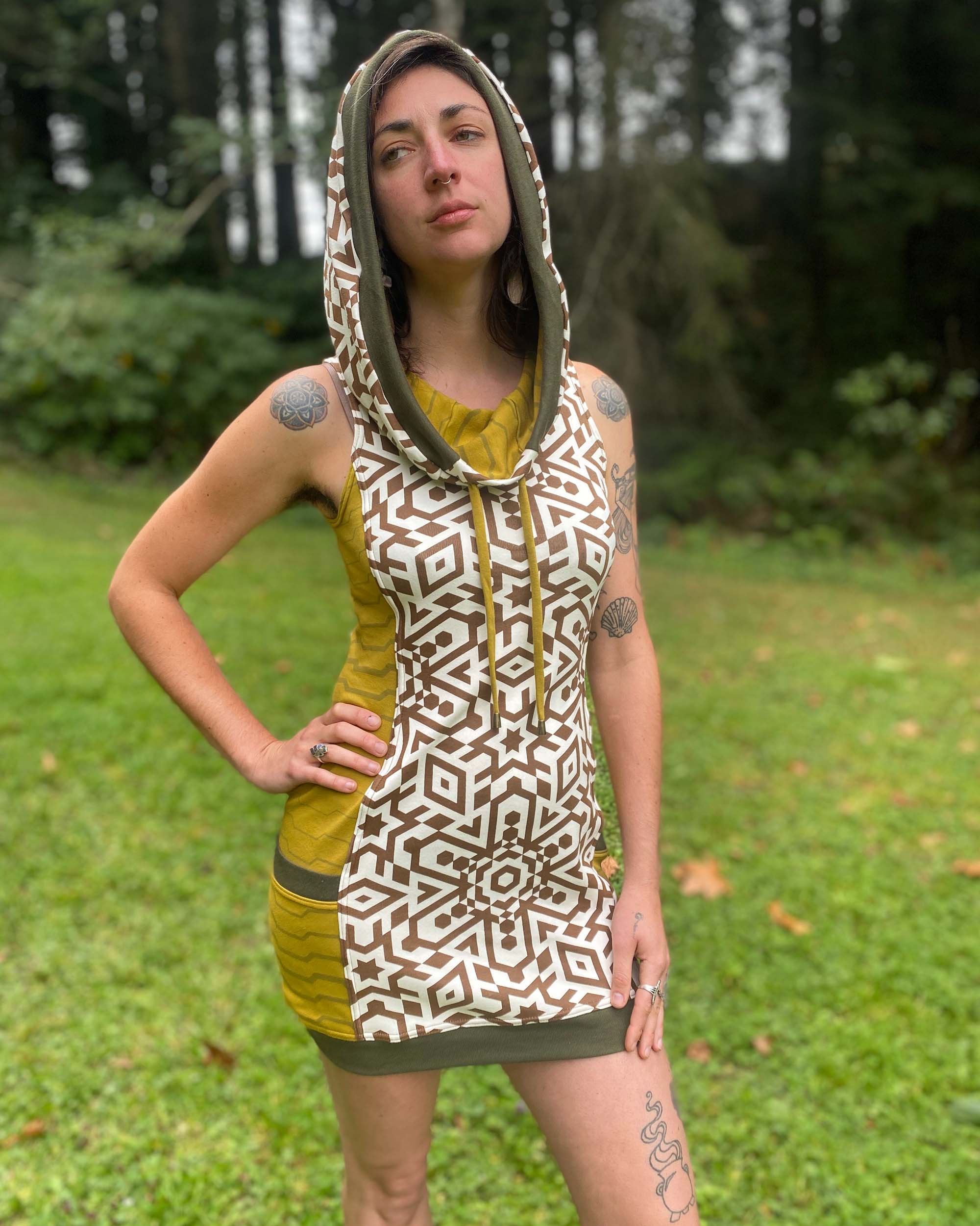 Organic cotton sleeveless hooded dress, natural color fabric with geometric print, front view of female model.