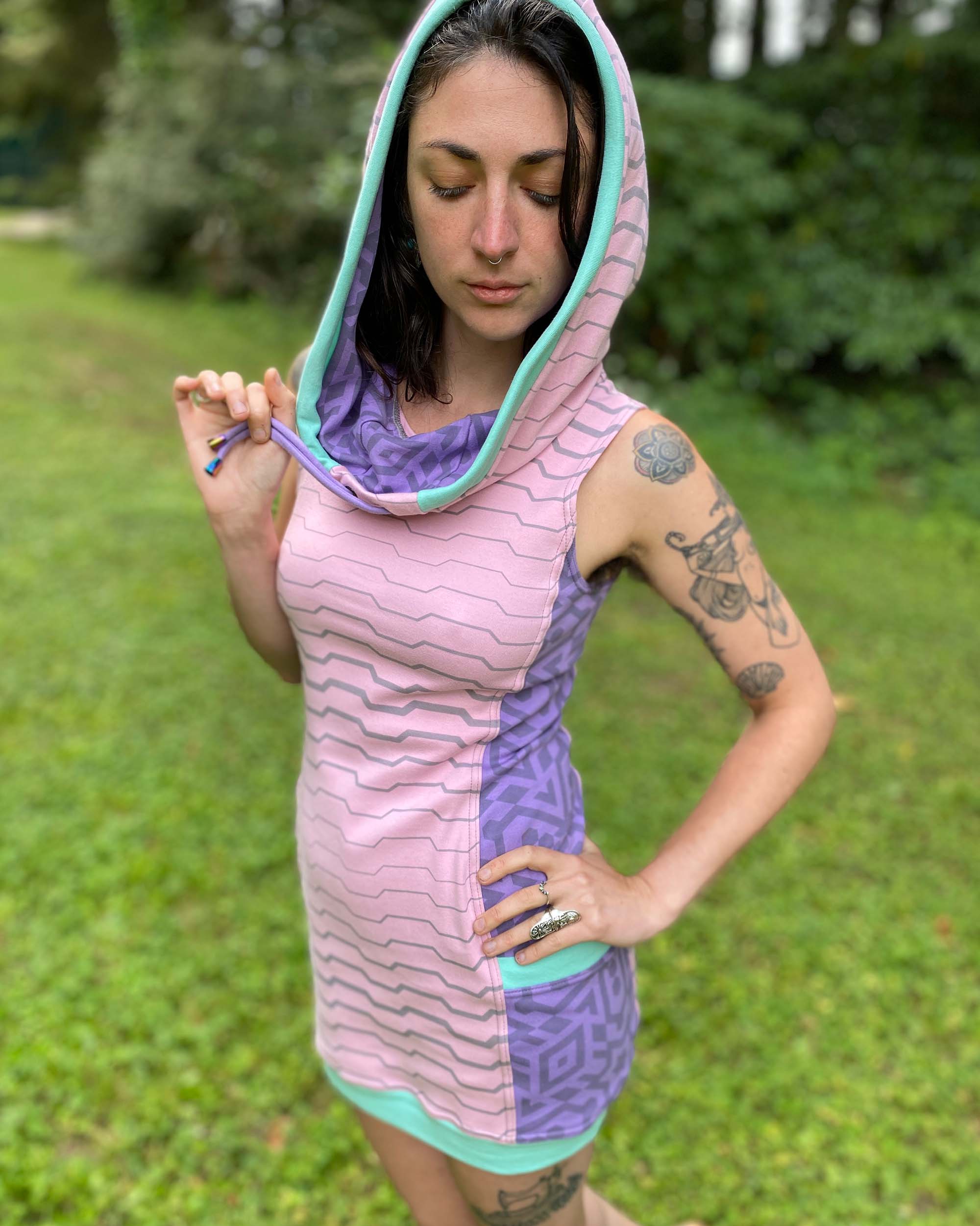 Organic cotton sleeveless hooded tunic dress, pink with lavender accents, front left side view on female model.