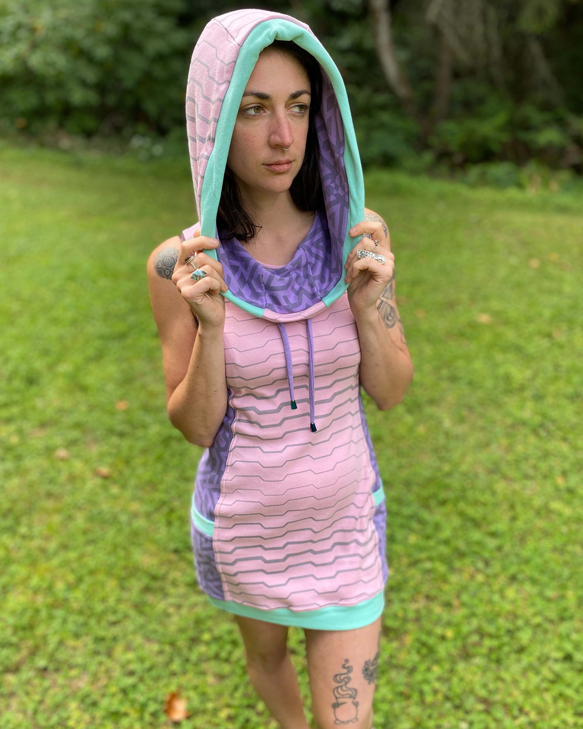 Organic cotton sleeveless hooded dress, pink with lavender colored accents, front view on female model, hood up.