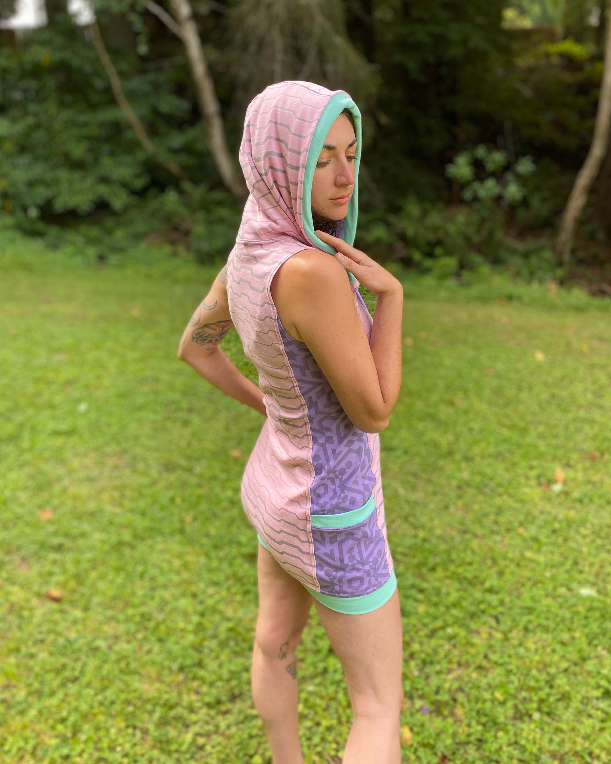 Organic cotton sleeveless hooded dress, pink with lavender colored accents, back side view on female model.