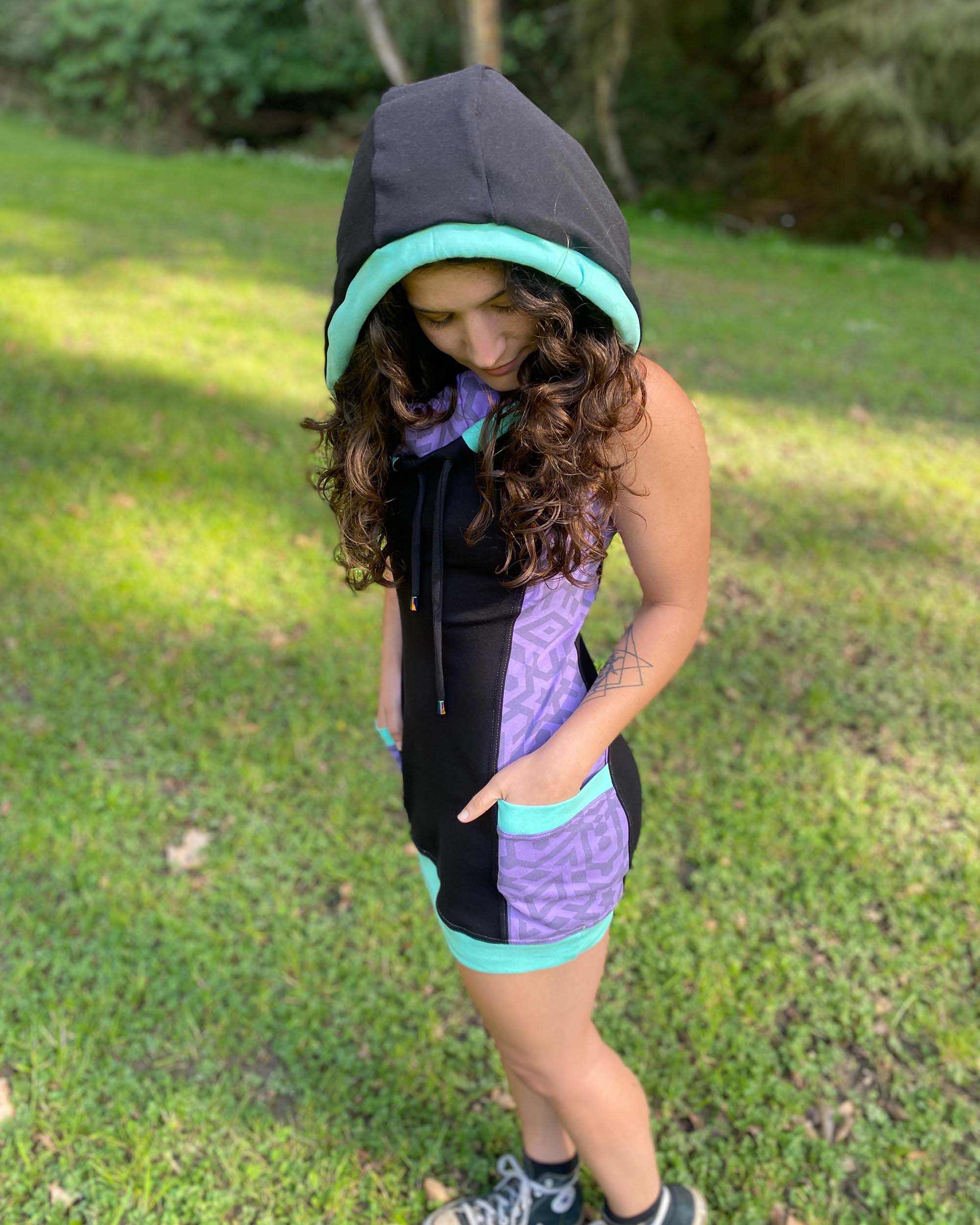 Organic cotton sleeveless hooded dress, black with lavender geo printed fabric, left front side view on female model.