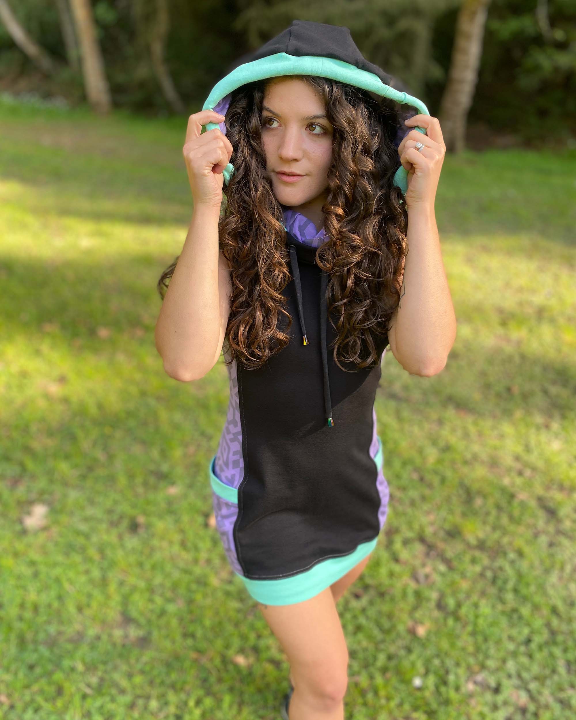 Organic cotton sleeveless hooded dress, black with lavender fabric accents, female model with hood up.