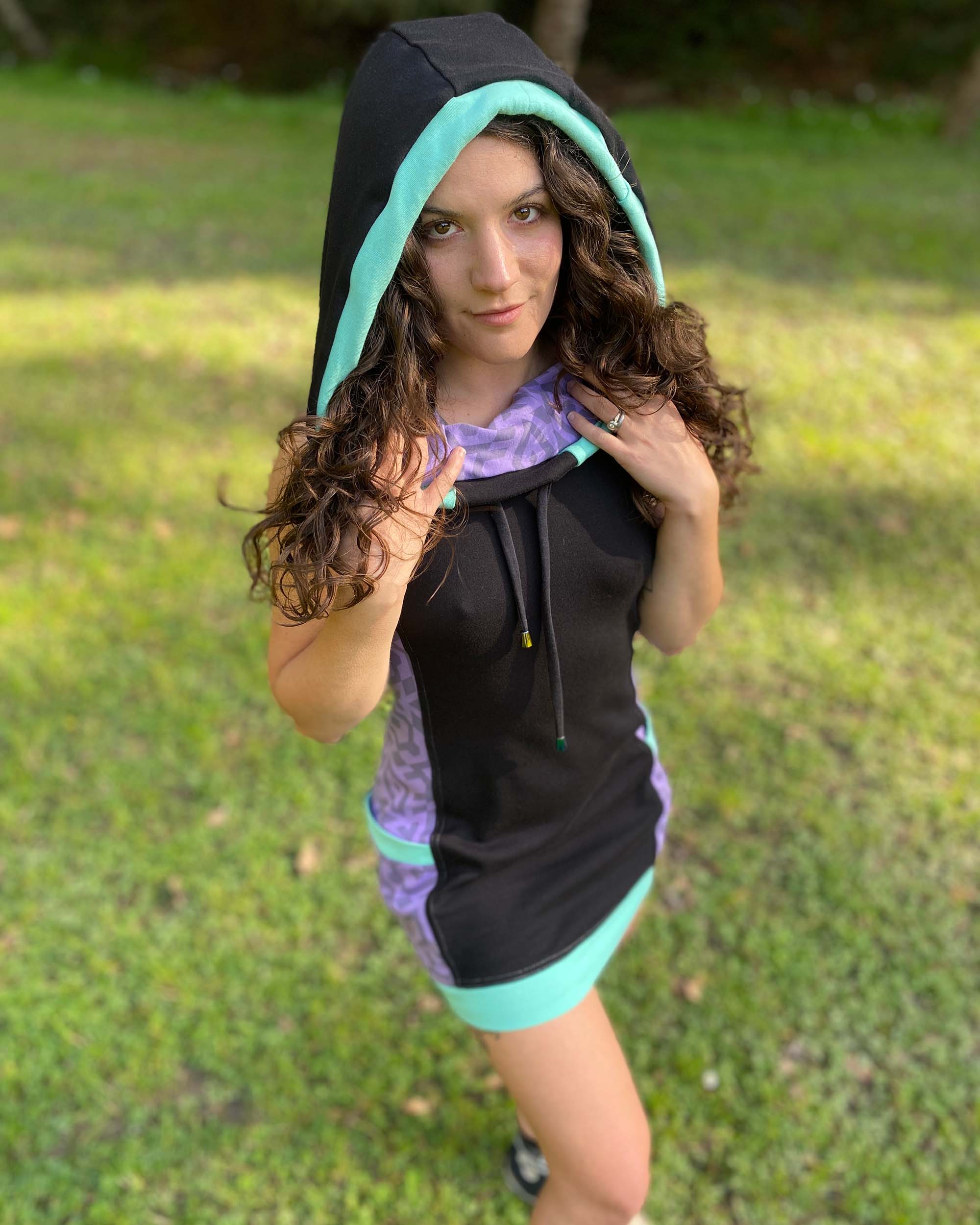 Organic cotton sleeveless hooded dress, black with lavender fabric accents, front view on female model.
