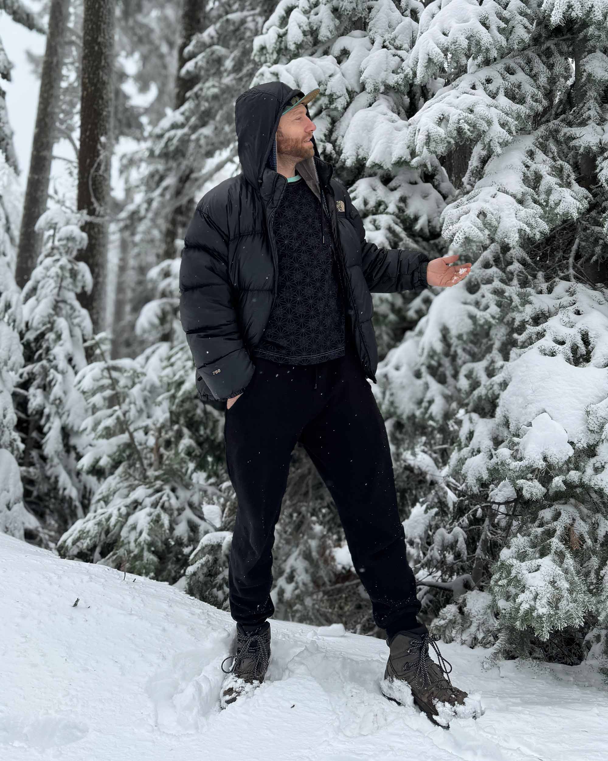 Organic cotton fleece joggers, solid black fabric, front view on male model with snowy trees.