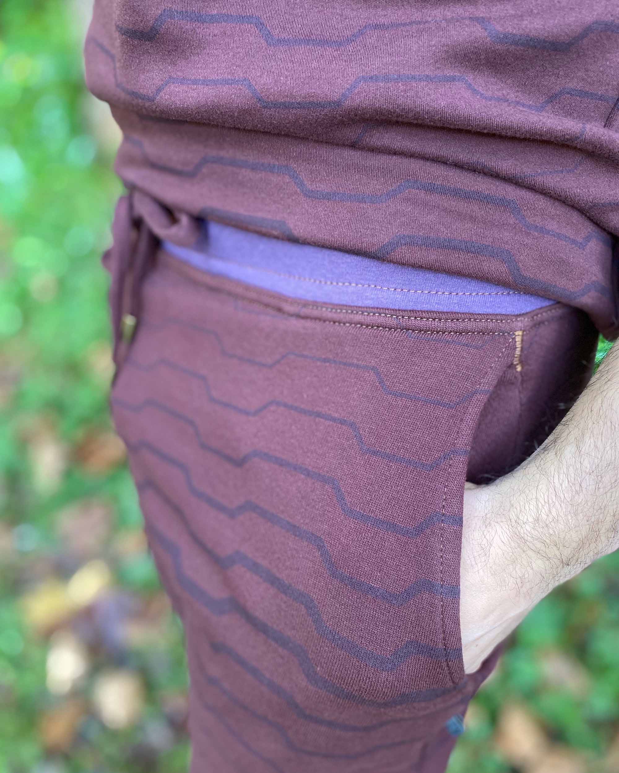 Organic cotton unisex joggers, reddish brown fabric with geometric all over print, detail view of pocket stitching.
