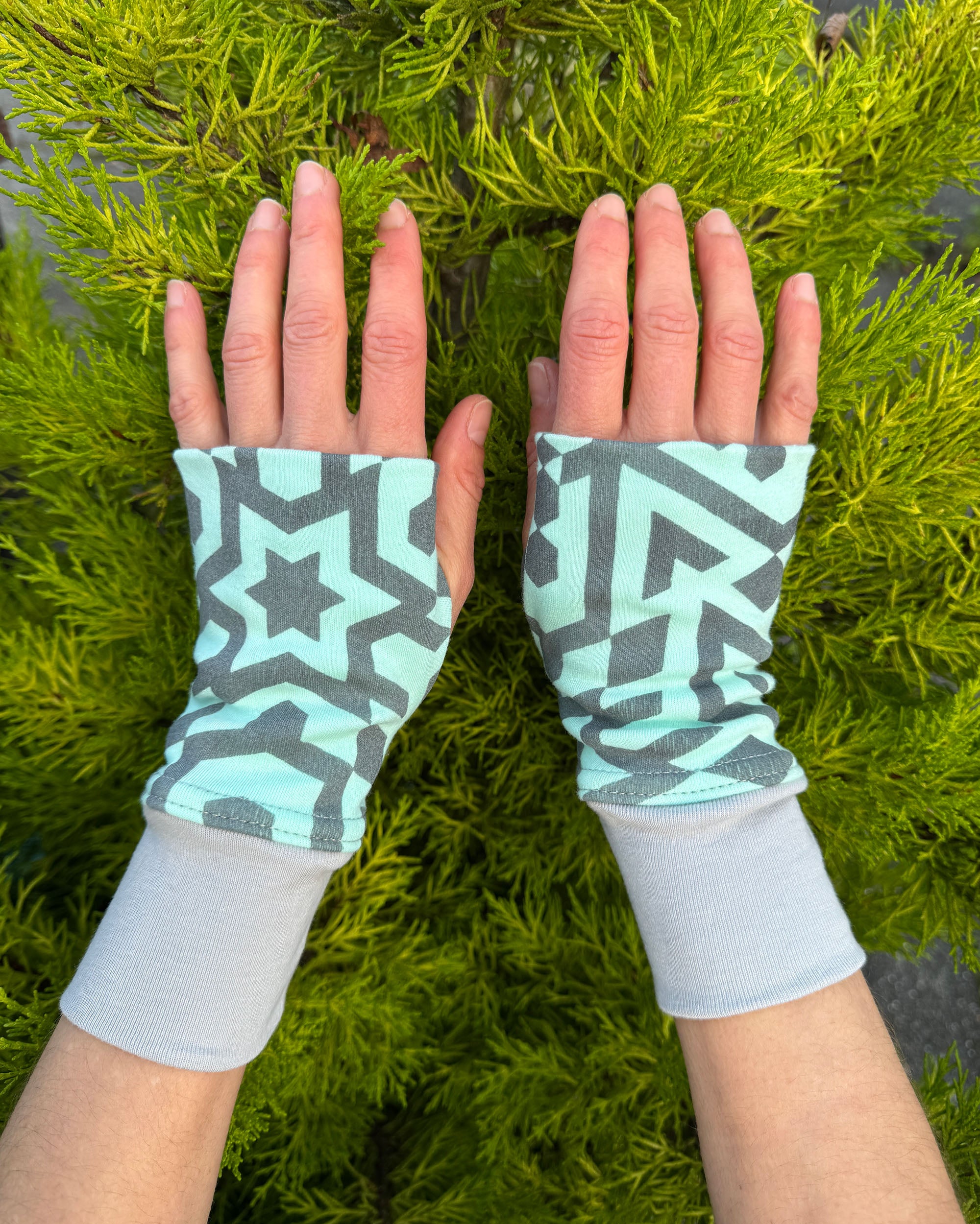 Female hands wearing organic cotton hand warmers, mint colored geo printed fabric.