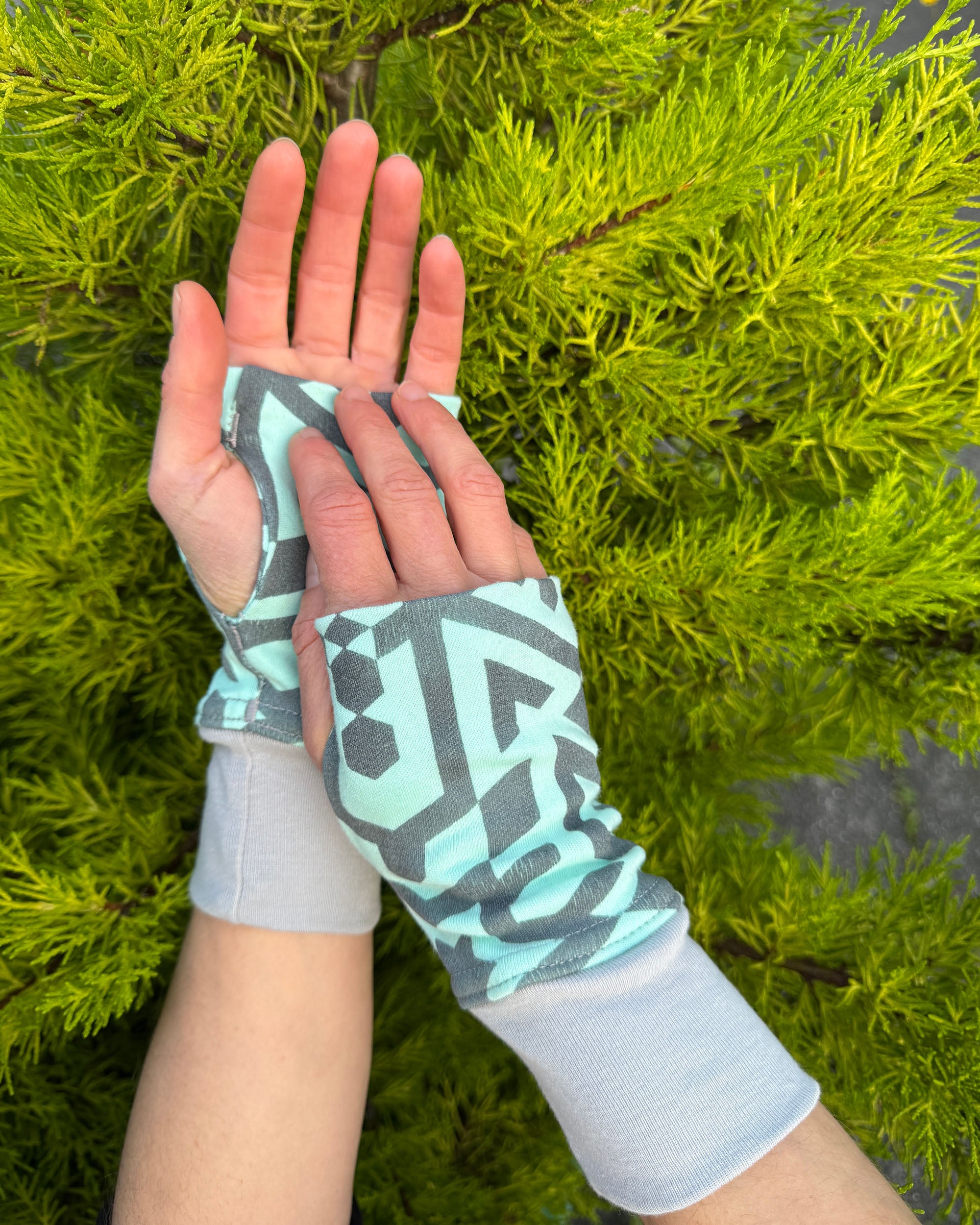 Hands wearing organic cotton hand warmers, mint colored geo printed fabric.