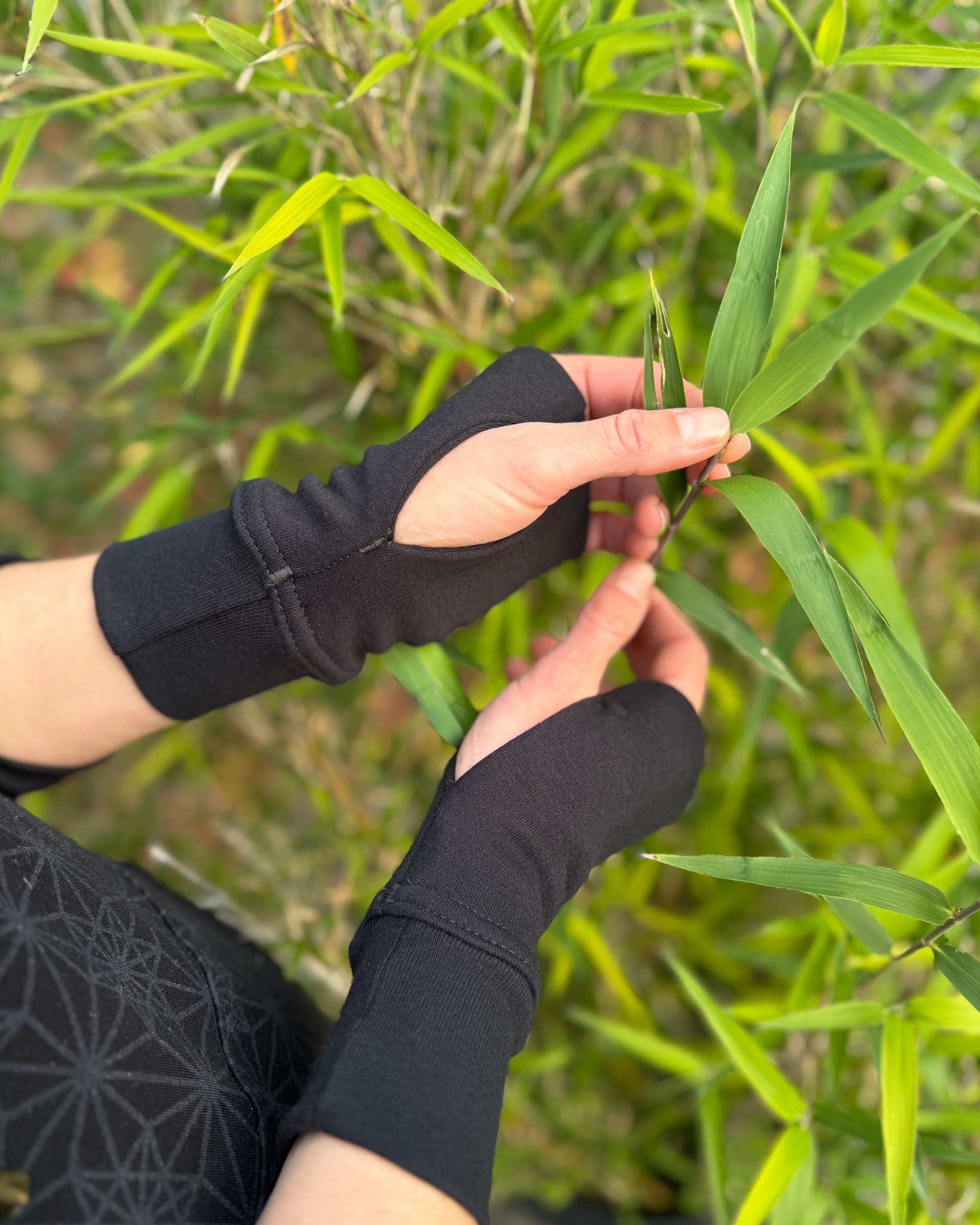 female hands wearing organic cotton wrist warmers with black fabric and natural background.