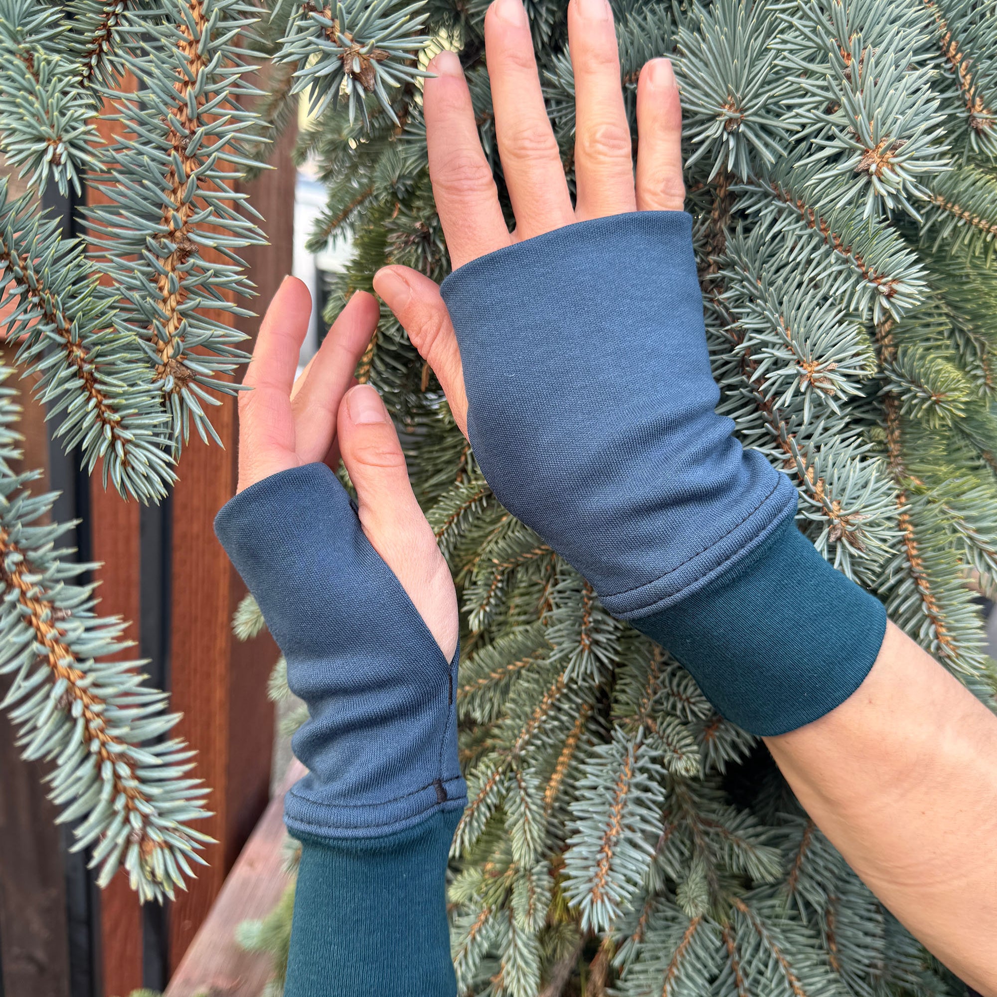Female hands wearing dark blue organic cotton hand warmers shown with natural background.