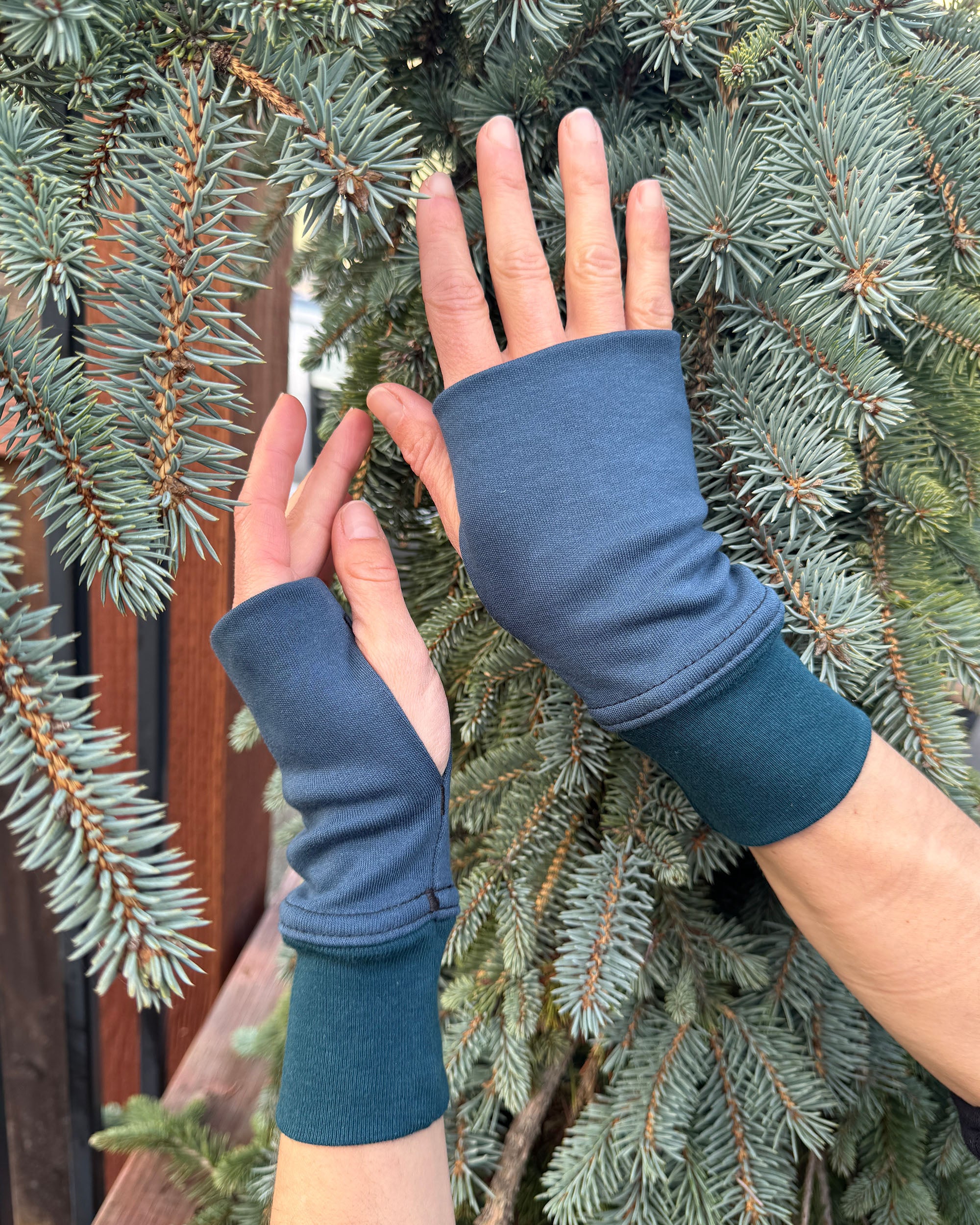Female hands wearing dark blue organic cotton hand warmers shown with natural background.