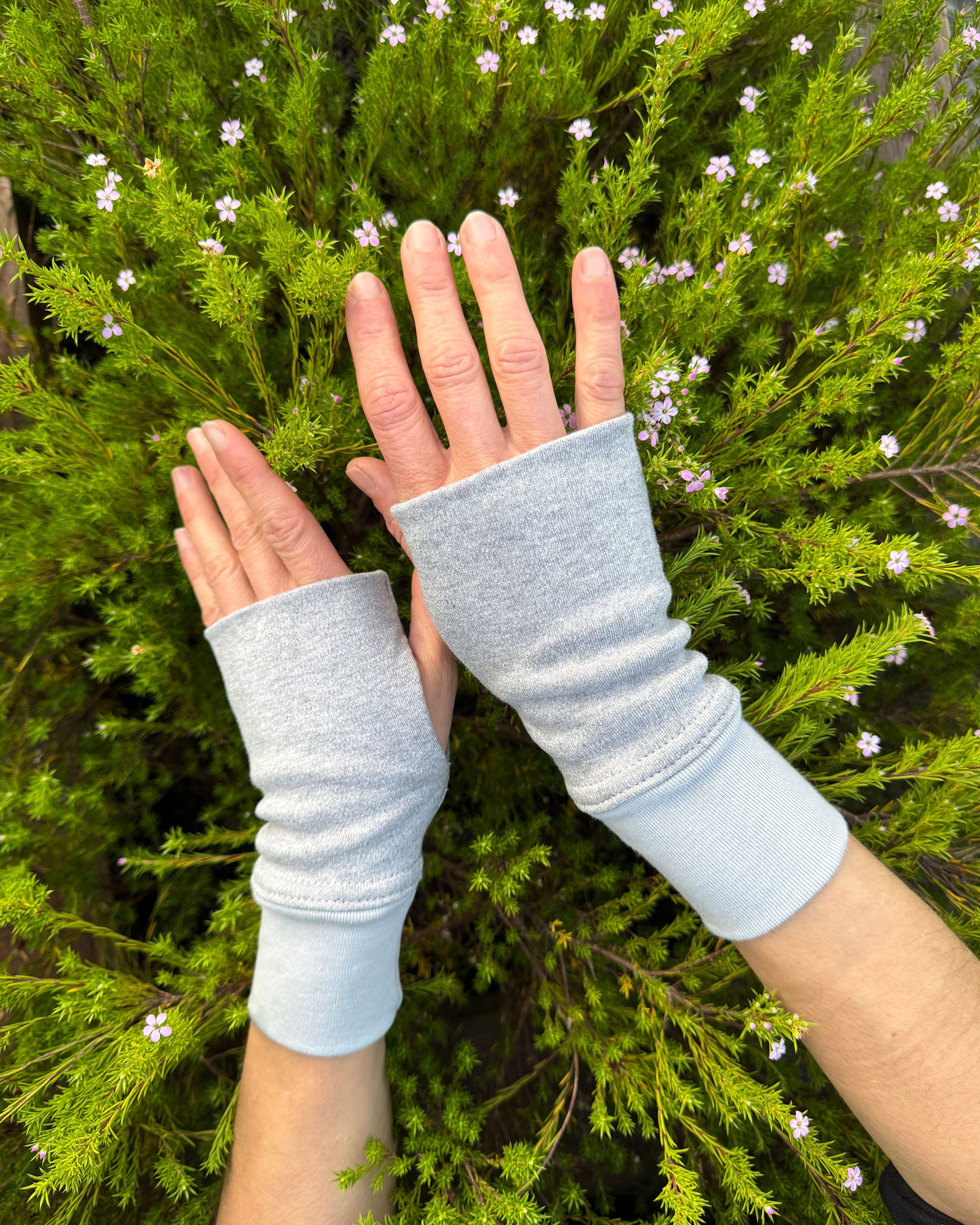 Female hands wearing solid grey organic cotton wrist warmers with a flowery background.
