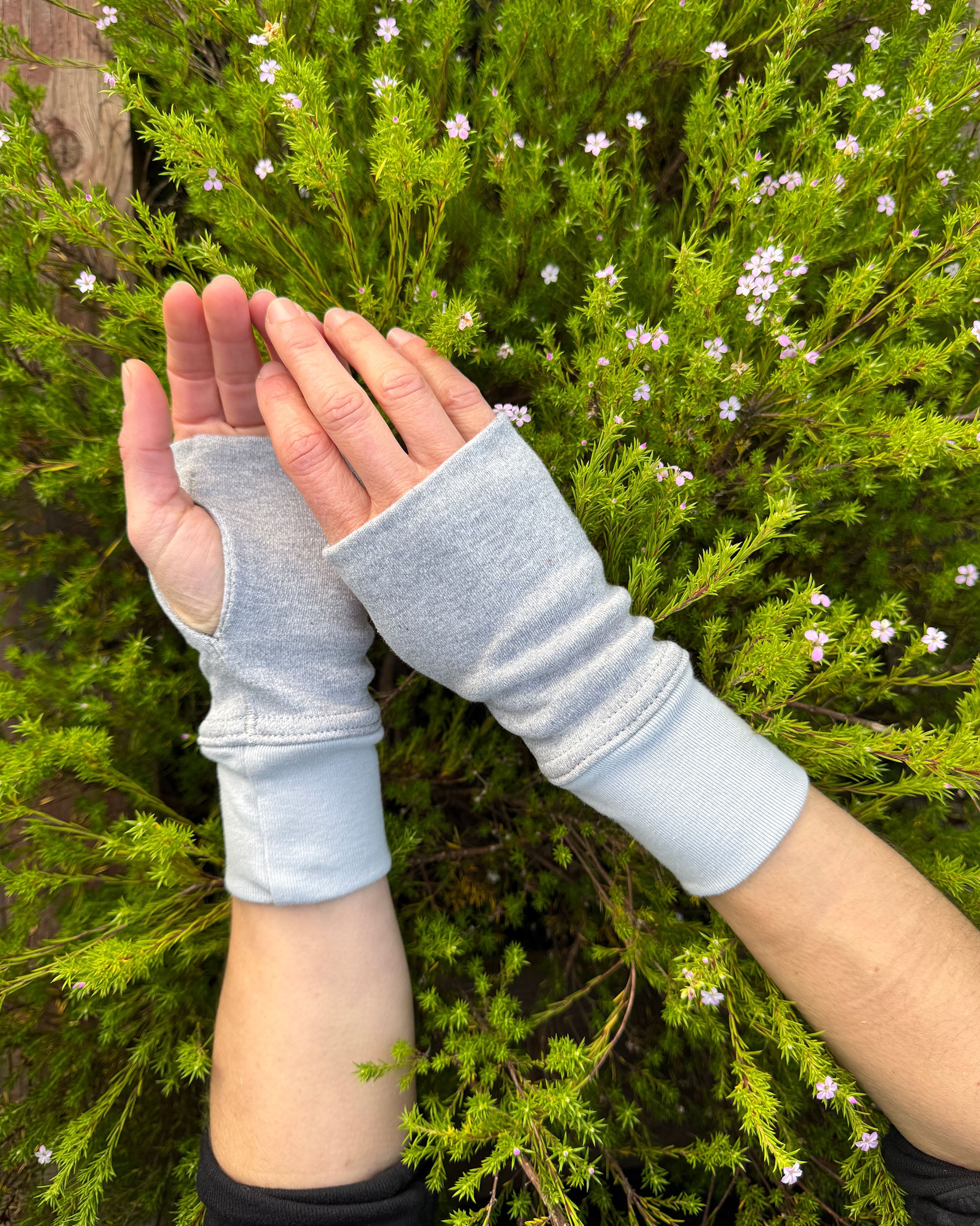 Hands wearing solid grey organic cotton hand warmers with a flowery background.