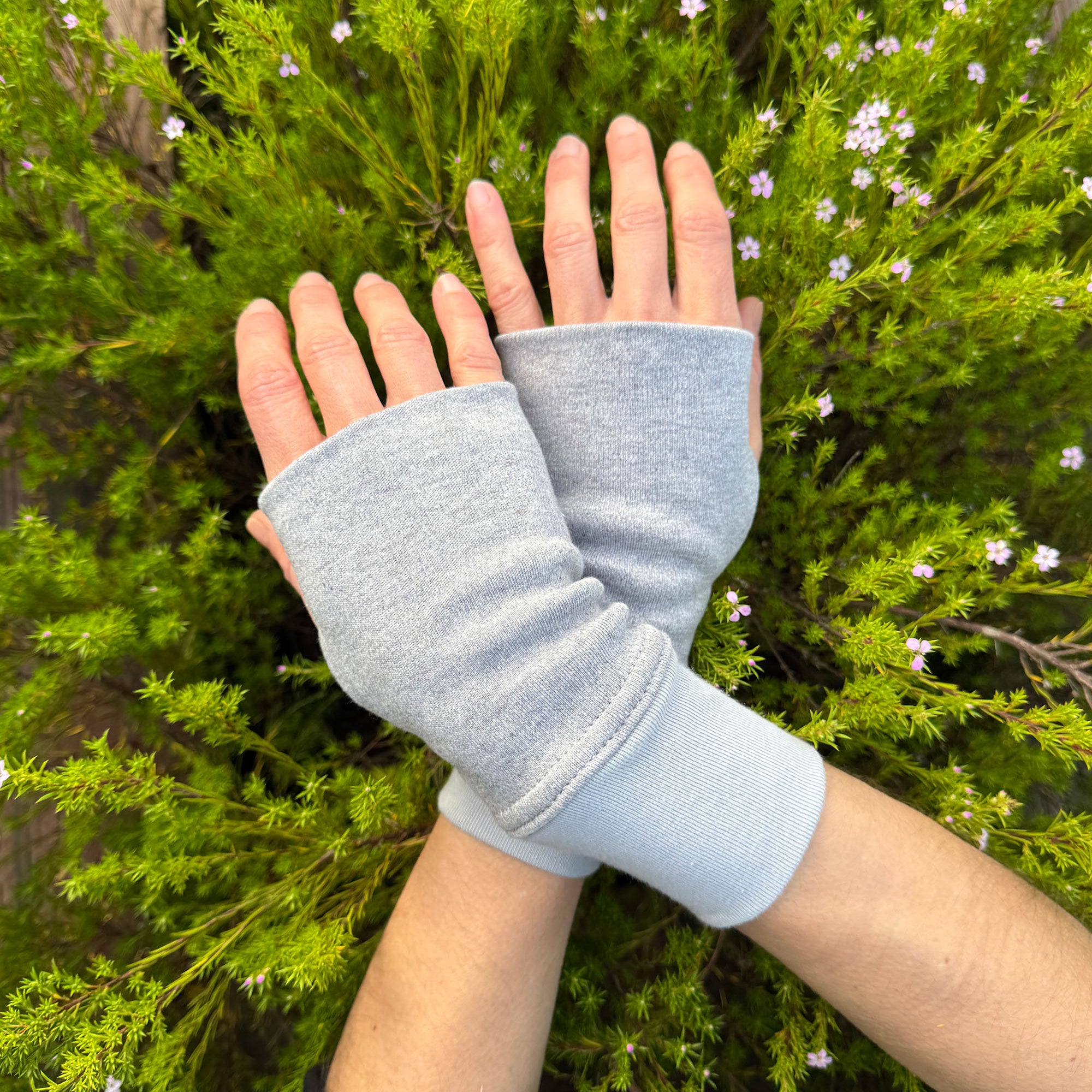 Female hands wearing solid grey organic cotton hand warmers with a flowery background.