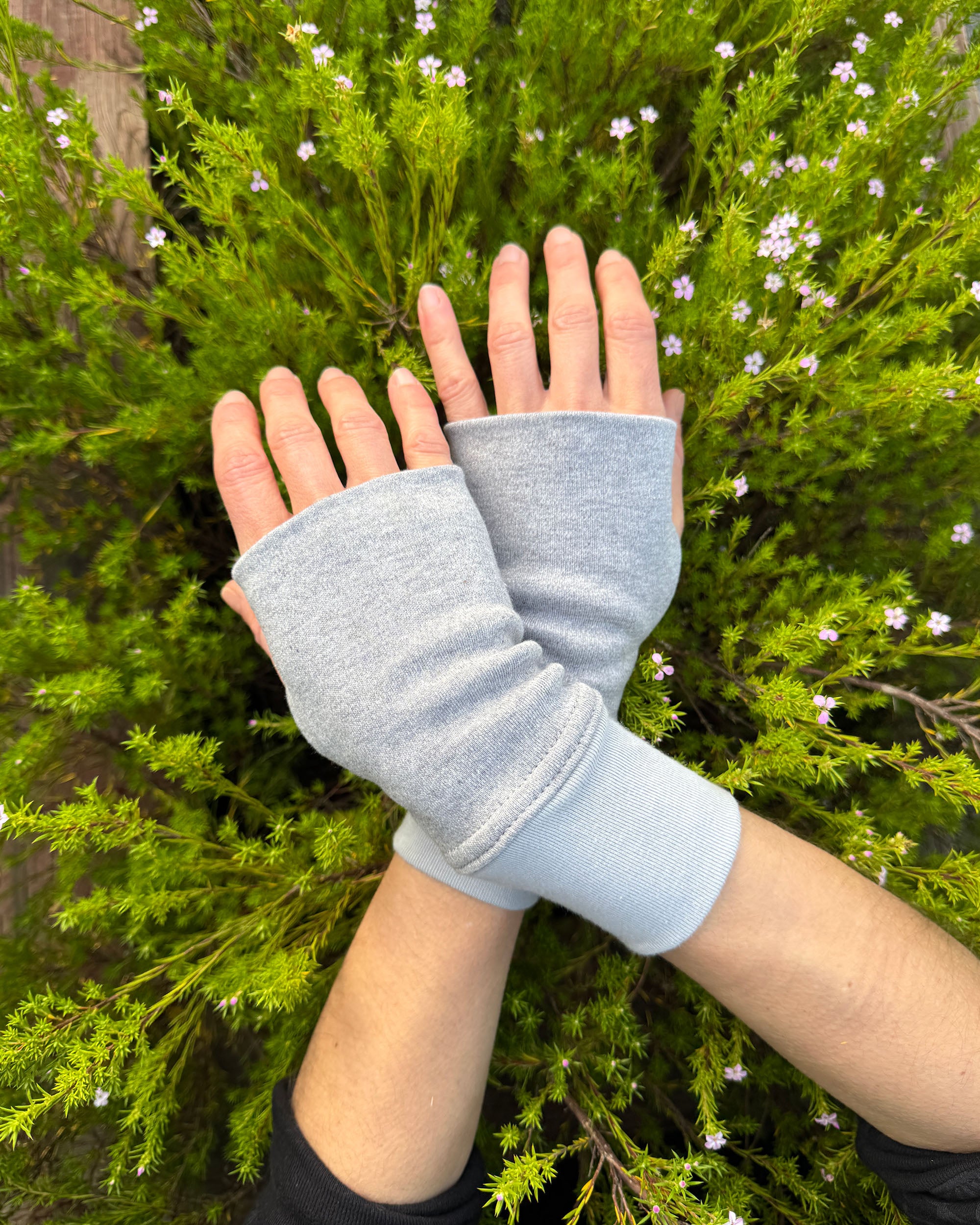 Female hands wearing solid grey organic cotton hand warmers with a flowery background.