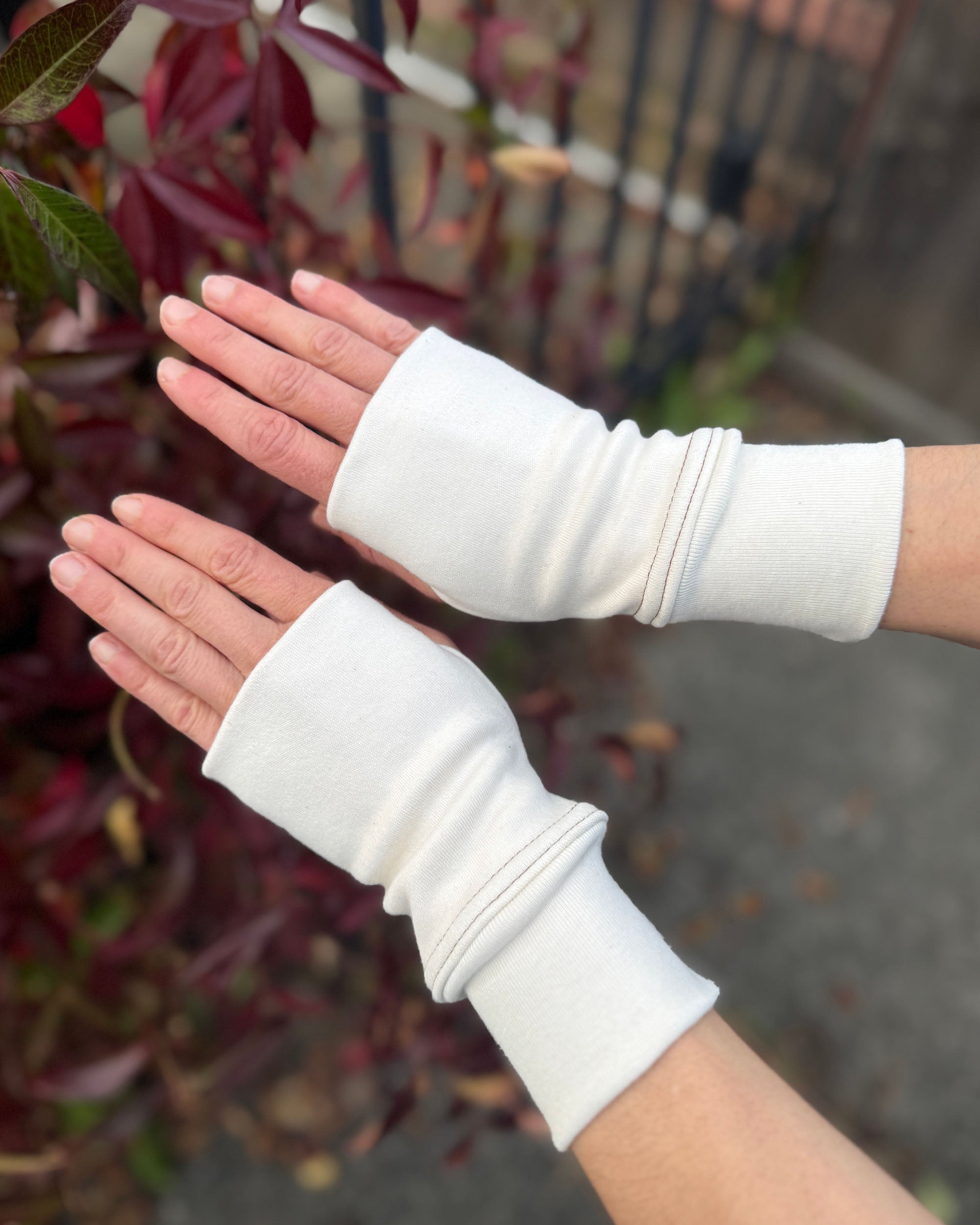 Female hands wearing organic cotton natural un-dyed hand warmers, with a natural background.
