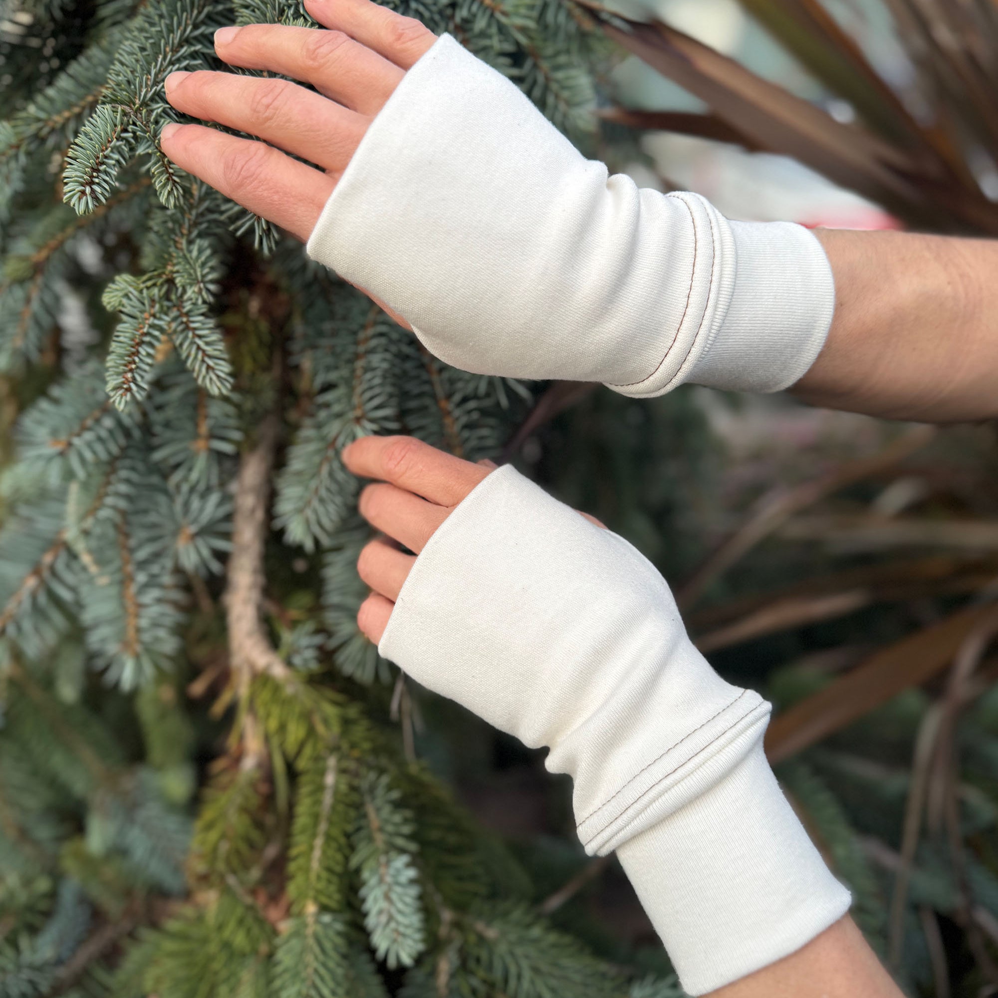 Female hands wearing organic cotton hand warmers, un-dyed fabric with natural background.