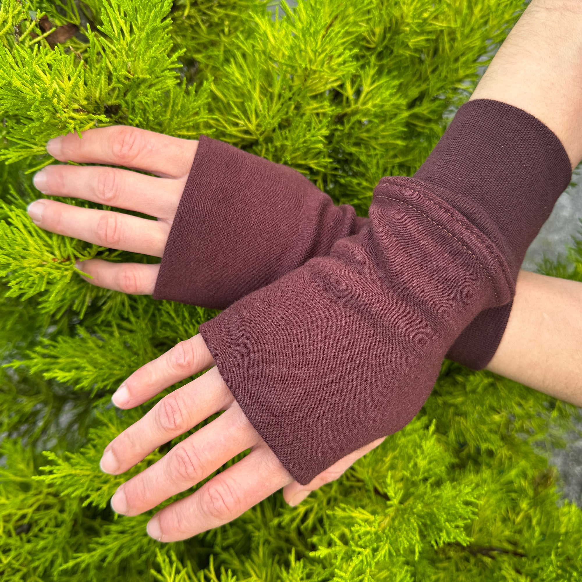 Female hands wearing organic cotton hand warmers, brown solid fabric with natural background.
