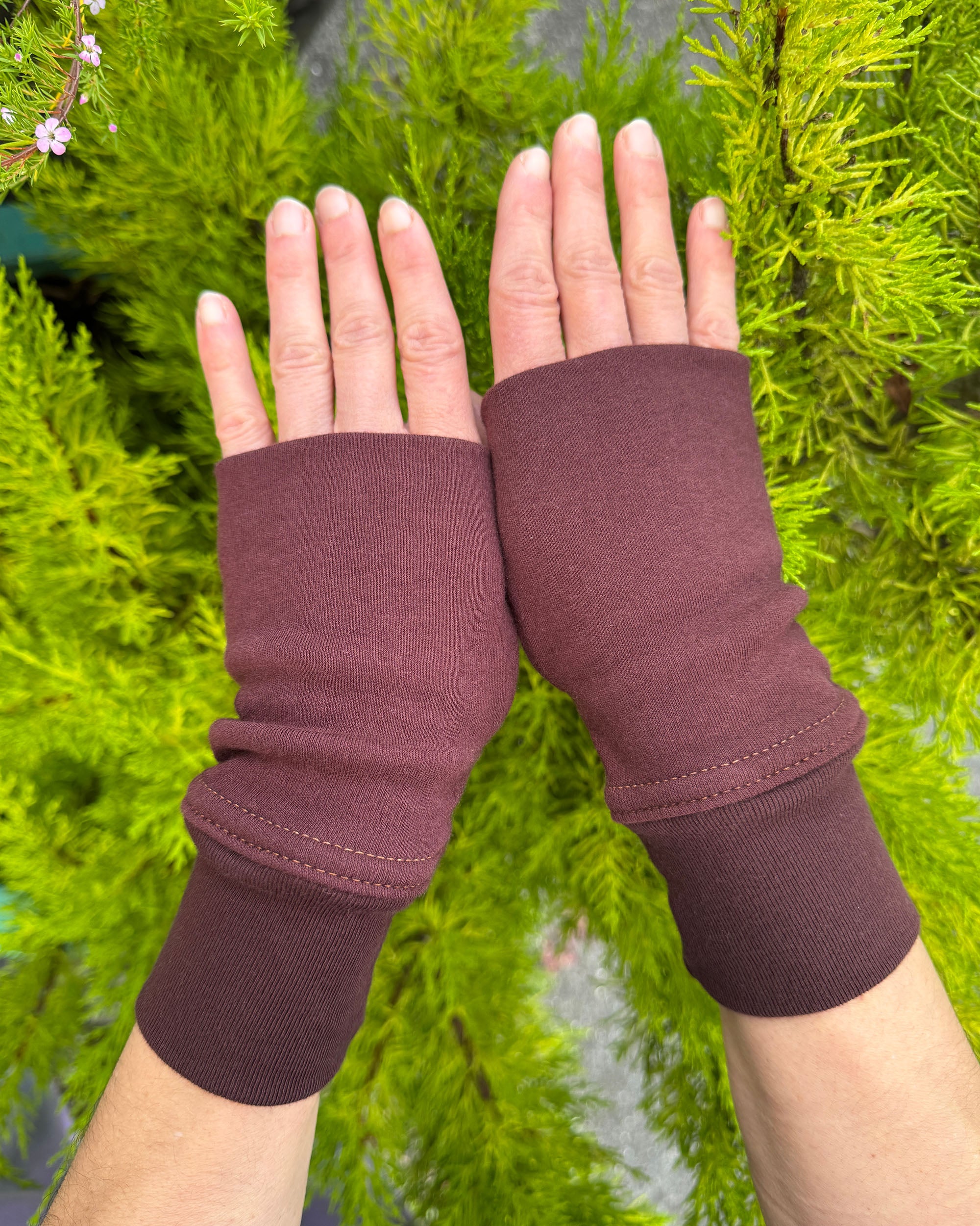 Female hands wearing organic cotton hand warmers, red brown colored fabric with natural background.