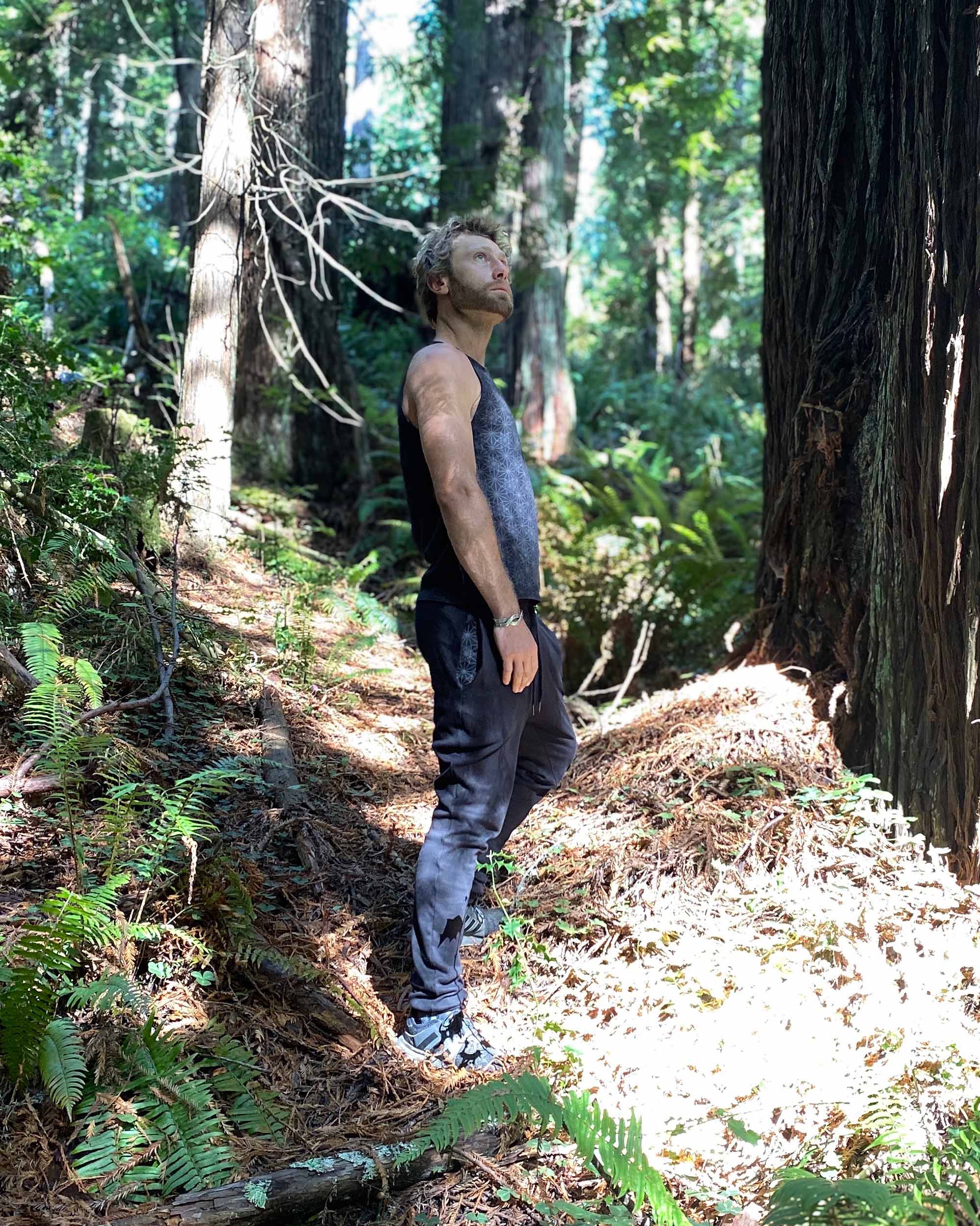Organic cotton unisex joggers, black fabric, right side full body view on male model with trees.