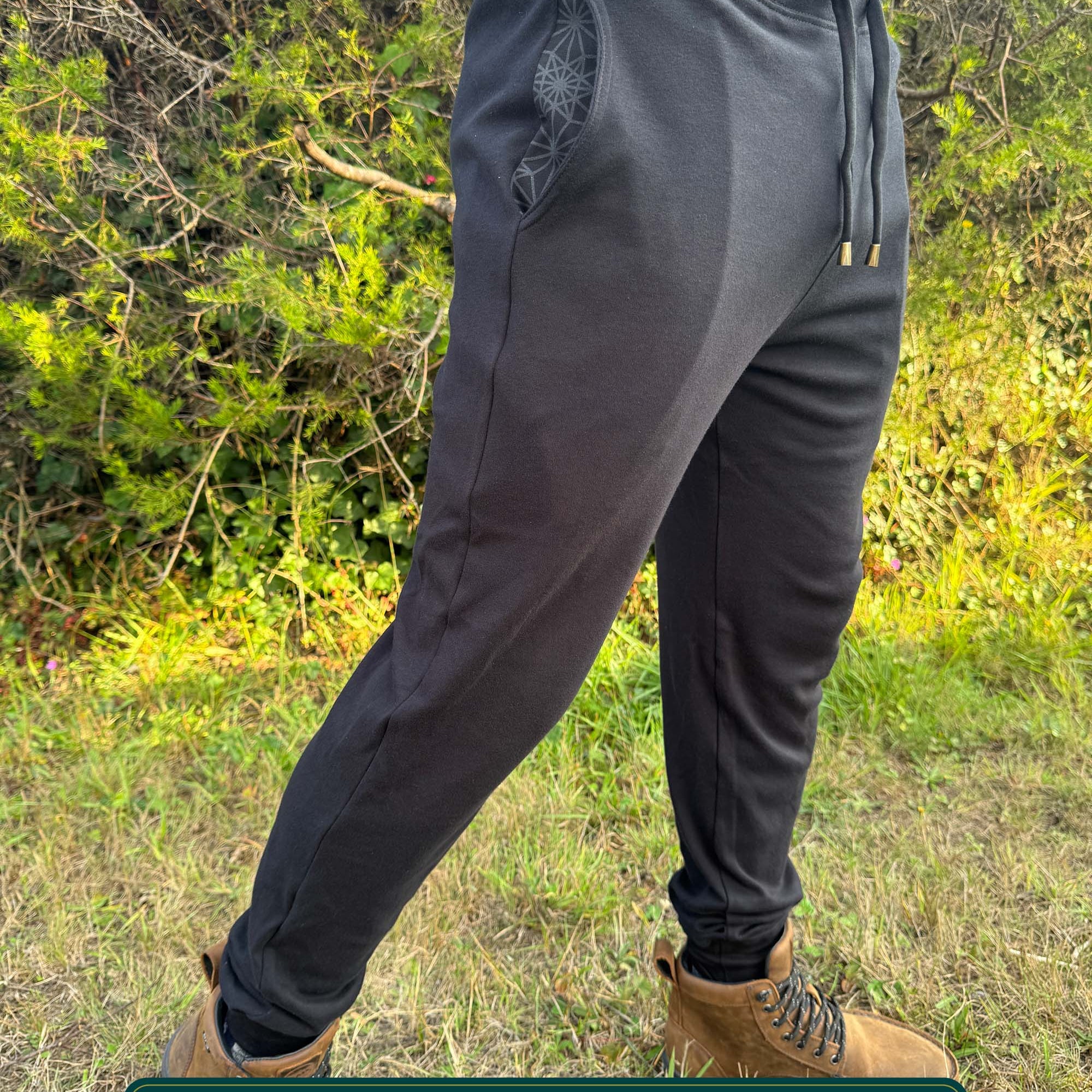 Organic cotton joggers, black fabric, right side full body view on male model in nature.