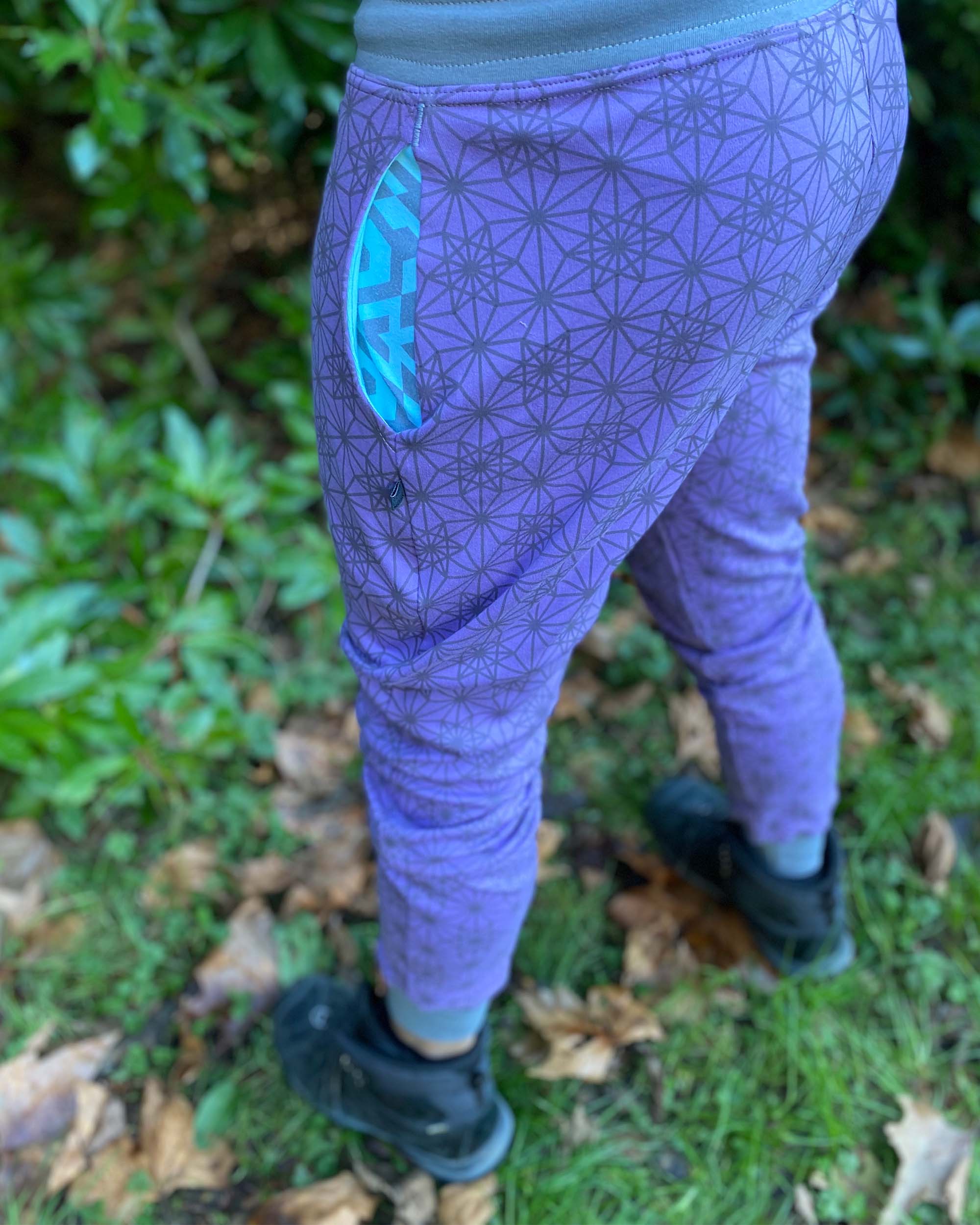 Organic cotton unisex joggers, lavender fabric with geometric print and blue accents, back side view on male model.
