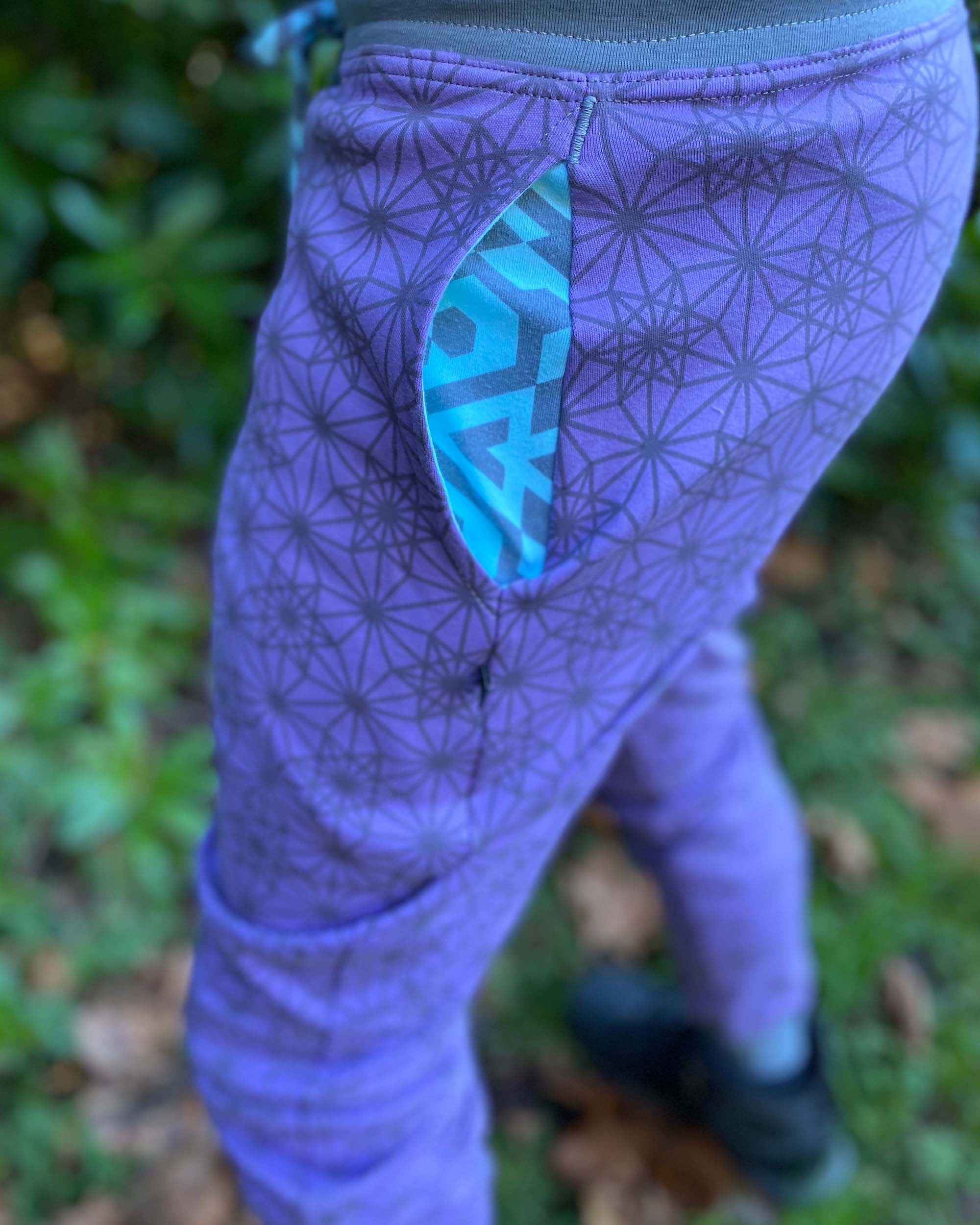 Organic cotton unisex joggers, lavender fabric with geometric print and blue accents, detail view of the pocket.