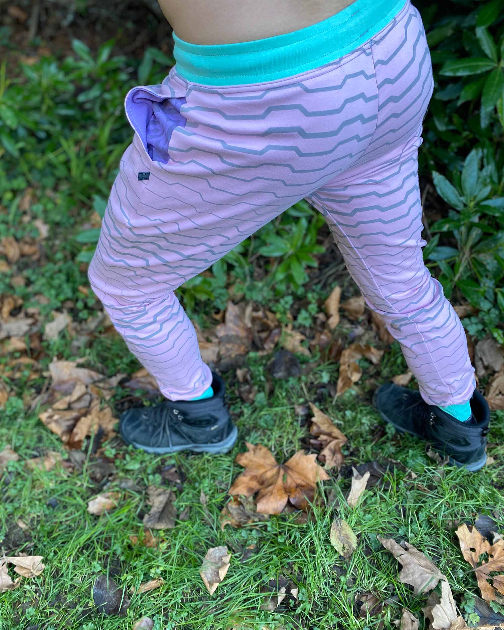 Organic cotton unisex joggers, pink fabric with geometric print and purple accents, back side view on male model.