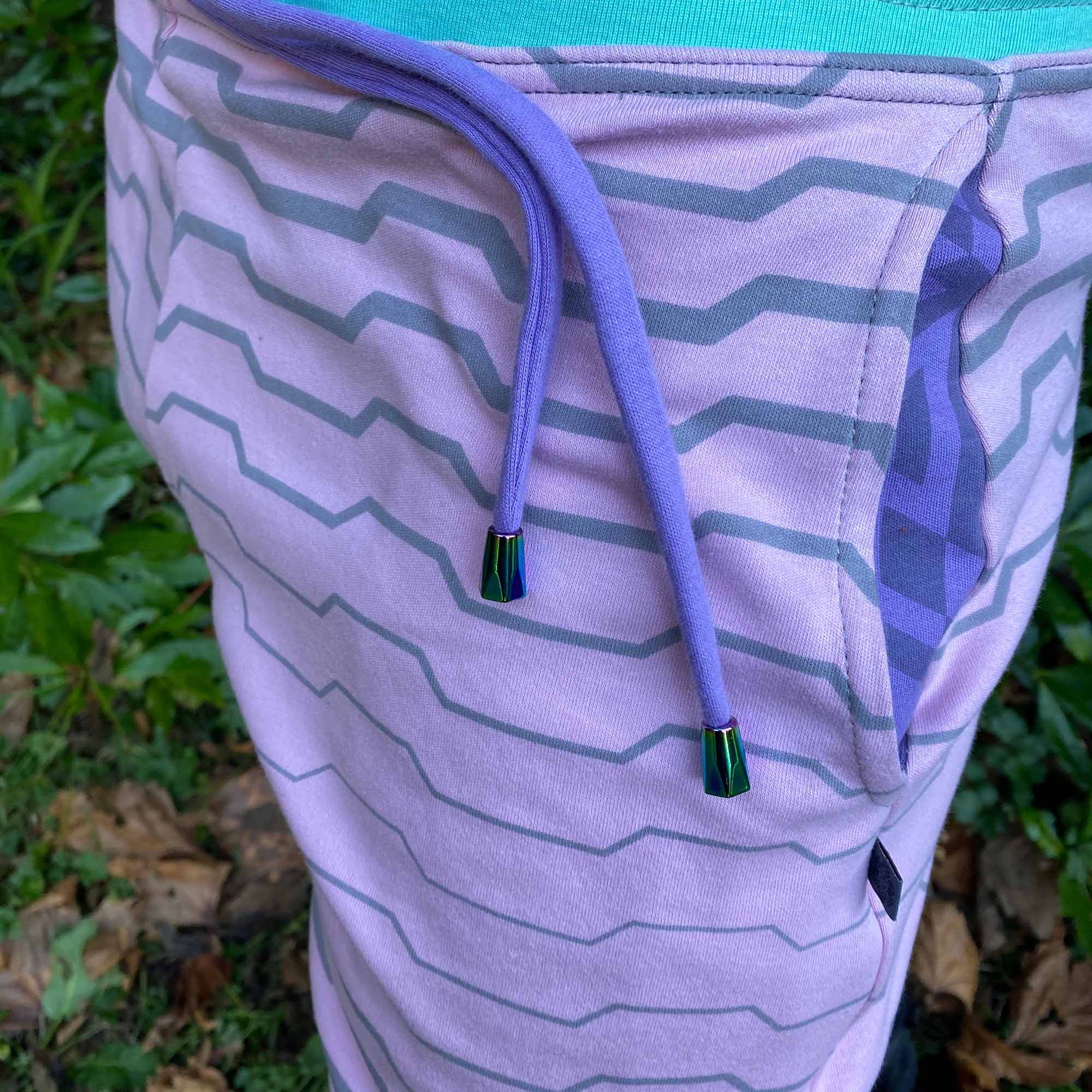 Organic cotton unisex joggers, pink fabric with geometric print and purple accents, detail side view.
