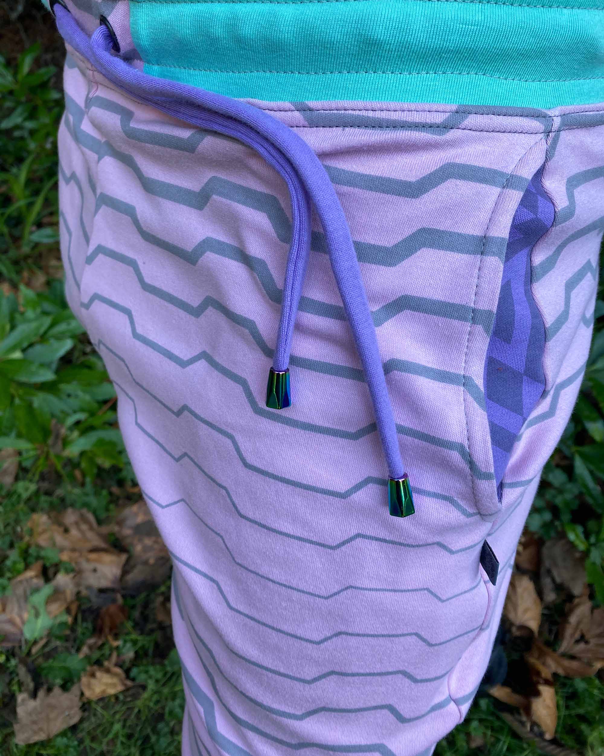 Organic cotton unisex joggers, pink fabric with geometric print and purple accents, detail side view.